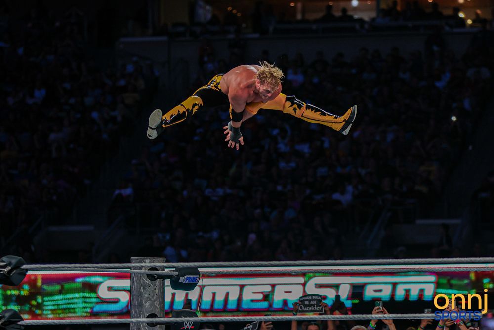WWE wrestler performs a dramatic mid-air leap in yellow attire at SummerSlam event.