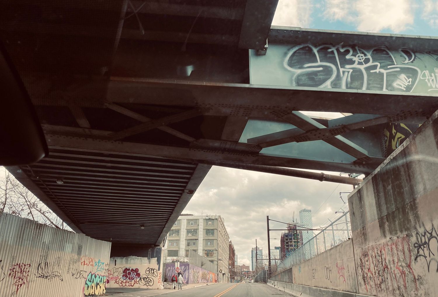 Urban underpass covered in colorful graffiti with city buildings visible in the background.