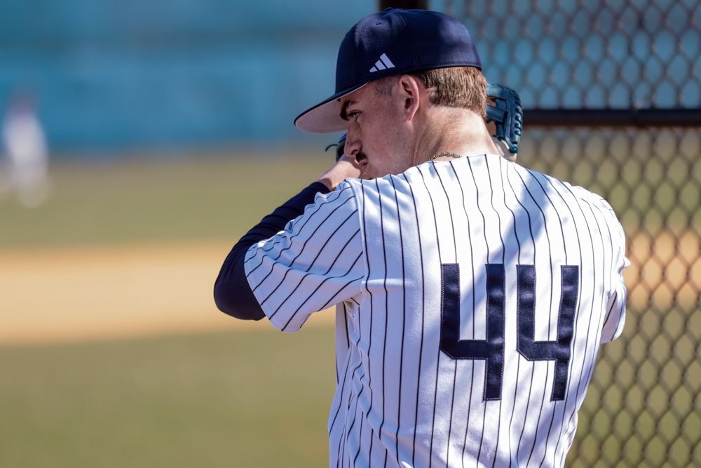 Baseball player wearing number 44 pinstripe uniform standing near dugout fence during daytime game.