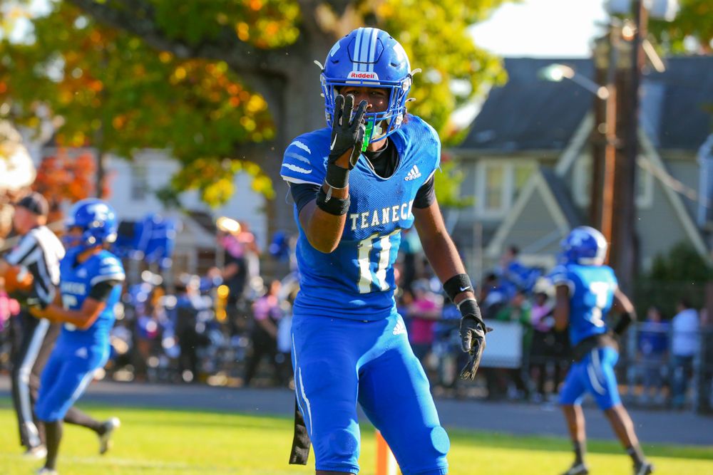 Teaneck football player number 11 in blue uniform celebrates on field during high school game.