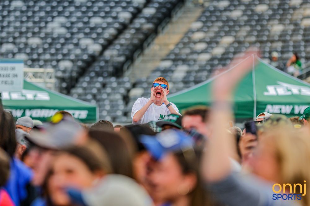 Excited NFL Jets fans cheer in a crowded stadium during a New York Jets game day event.