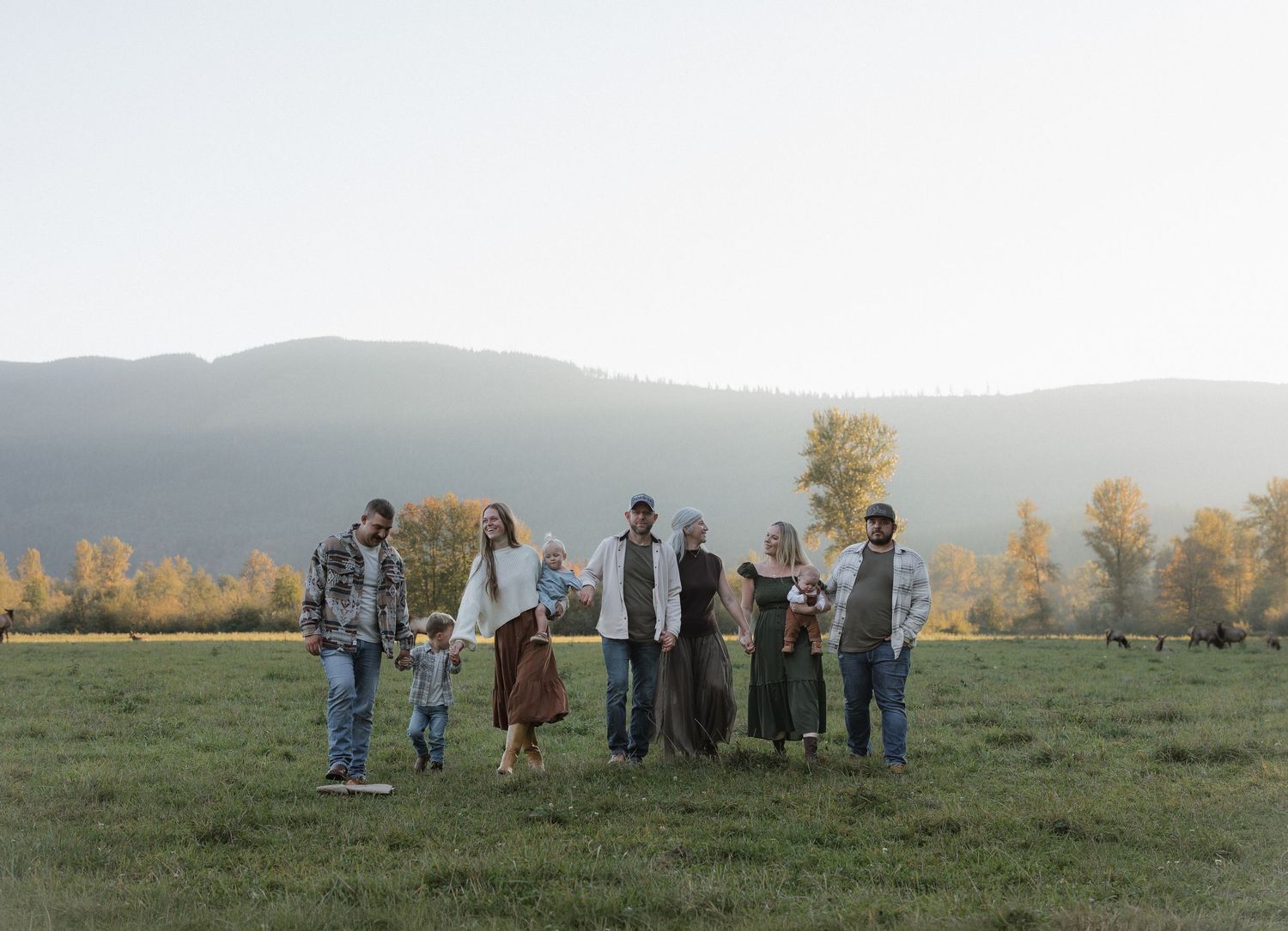 A group of eight people standing in a green meadow with mountains and autumn trees in the background.