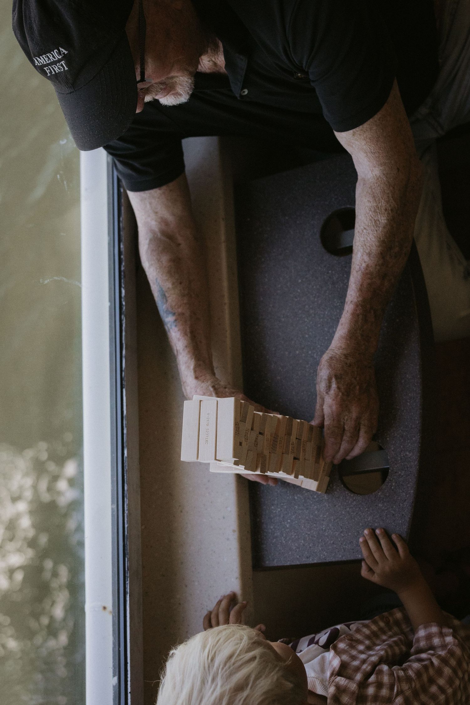 Aerial view of an adult and child playing Jenga on a gray table near a window.