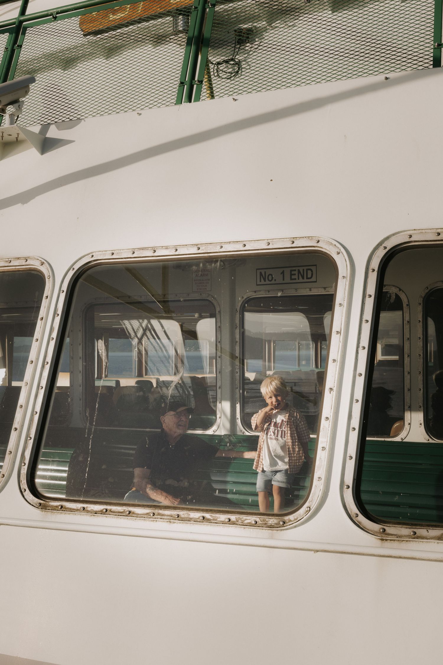 Two children visible through windows of a vintage white ferry boat labeled No. 1 End, with green interior seating.