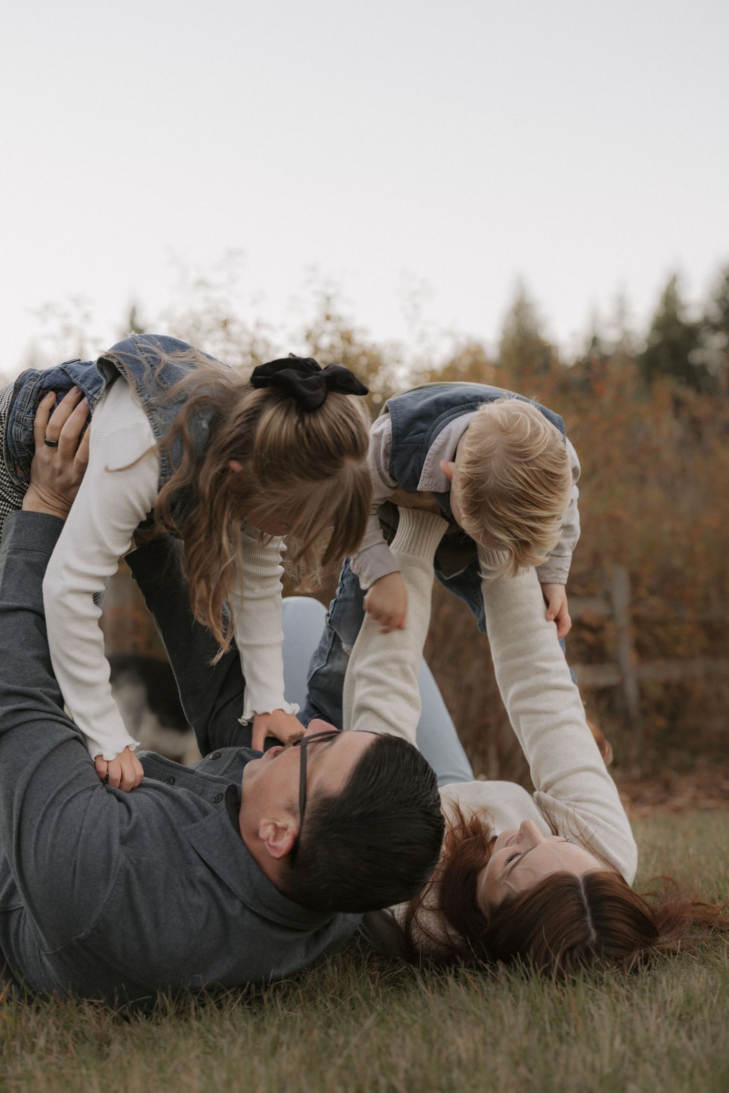 Parents lying on grass playfully lifting two young children in an outdoor autumn family photo session.
