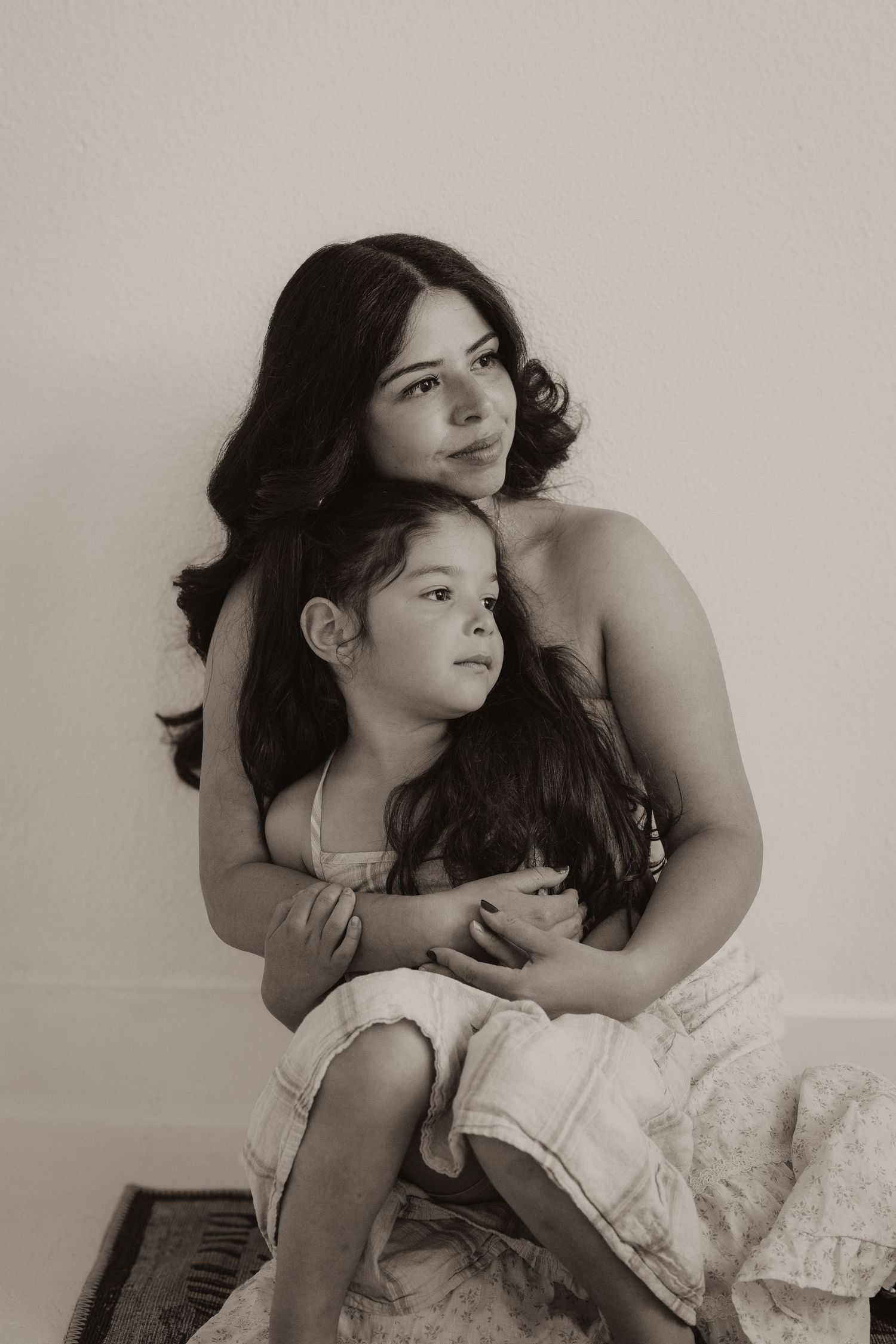 A mother tenderly holds her young daughter in a sepia-toned portrait photo.
