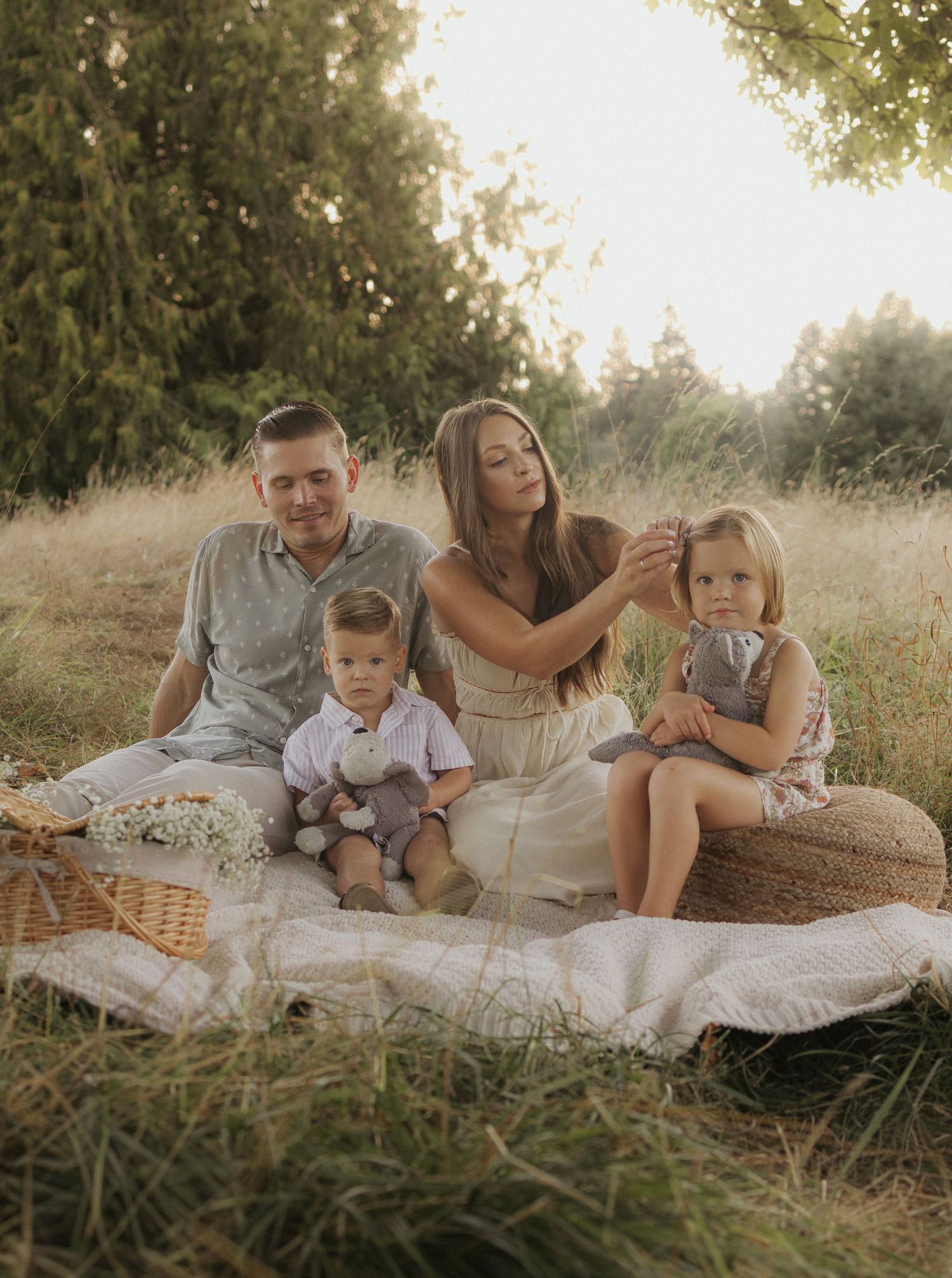 Family of four enjoying a golden hour picnic in a meadow, with two young children sitting on a blanket surrounded by nature.