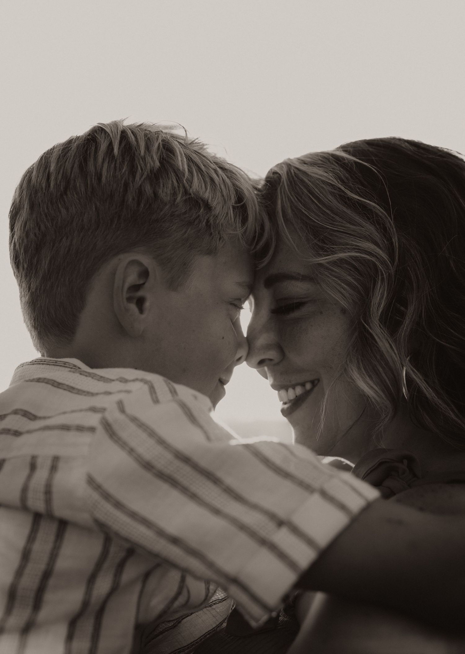 Black and white photo of a smiling woman and young boy touching foreheads in a tender, loving embrace.
