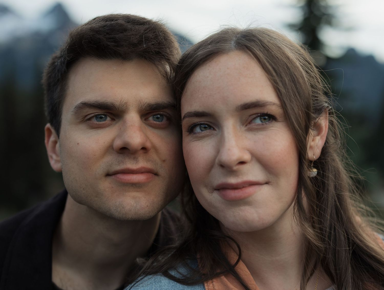 A young couple poses closely together outdoors with misty mountains in the background.