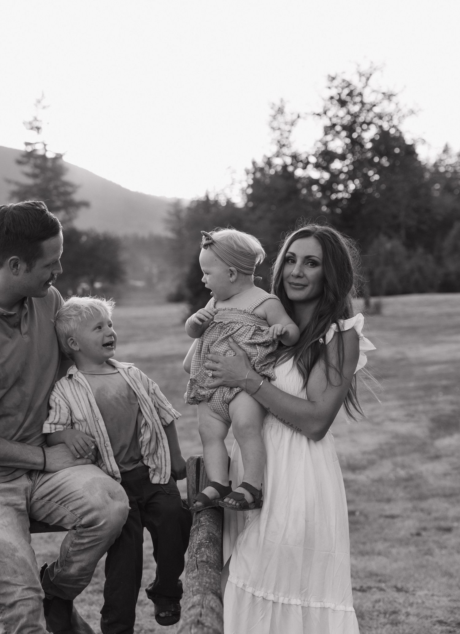 Black and white family photo of parents with two young children in a scenic outdoor field with trees and mountains.