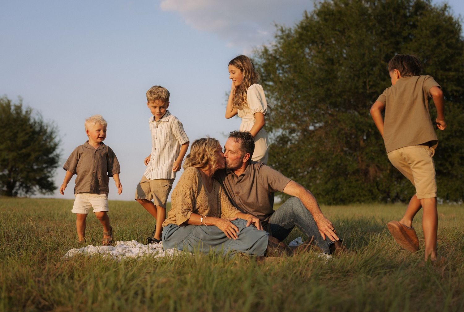 Family enjoying outdoor time together, parents sitting in grass while children play around them on a sunny day.