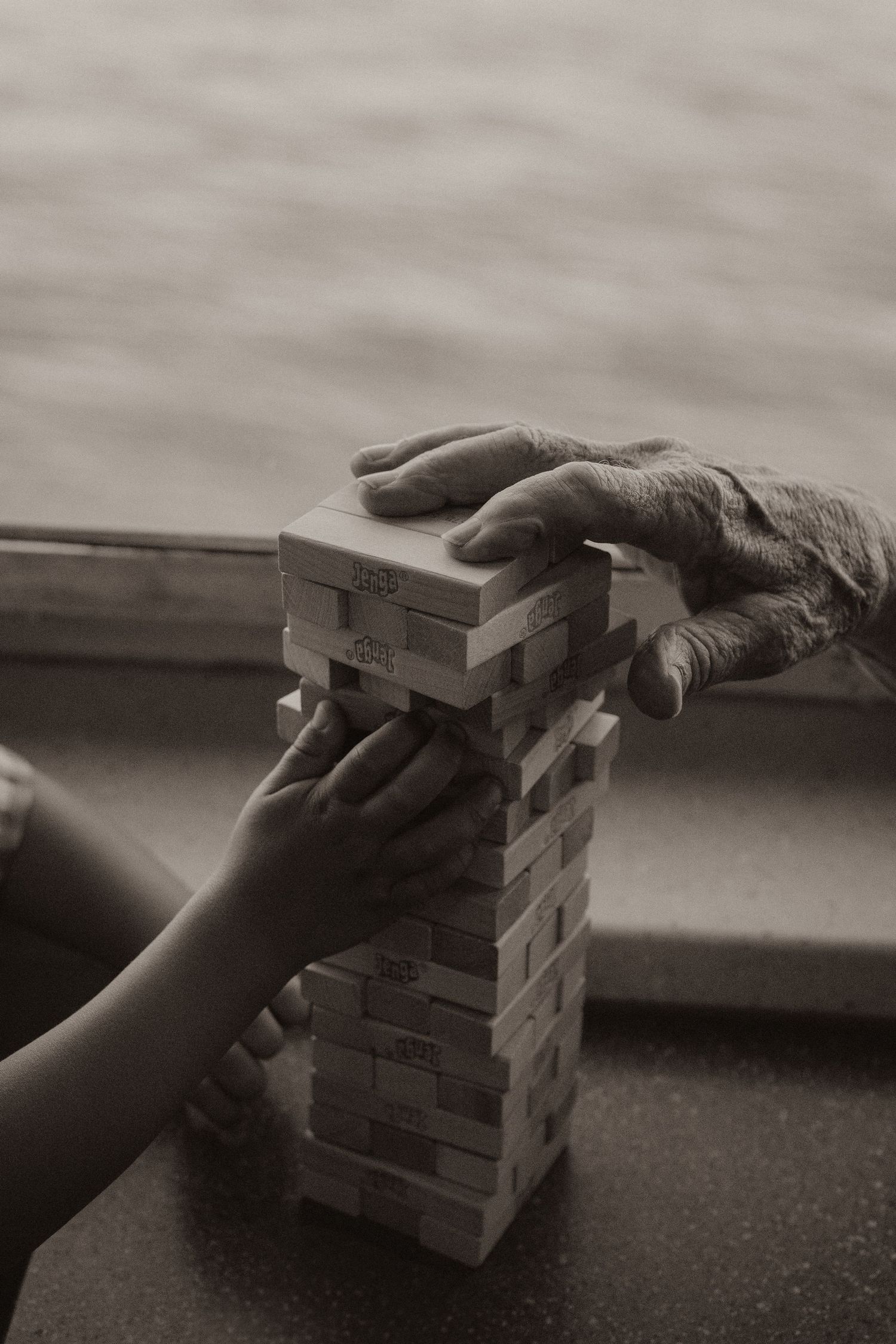 An elderly hand and a child's hand play Jenga together in a heartwarming black and white photo.