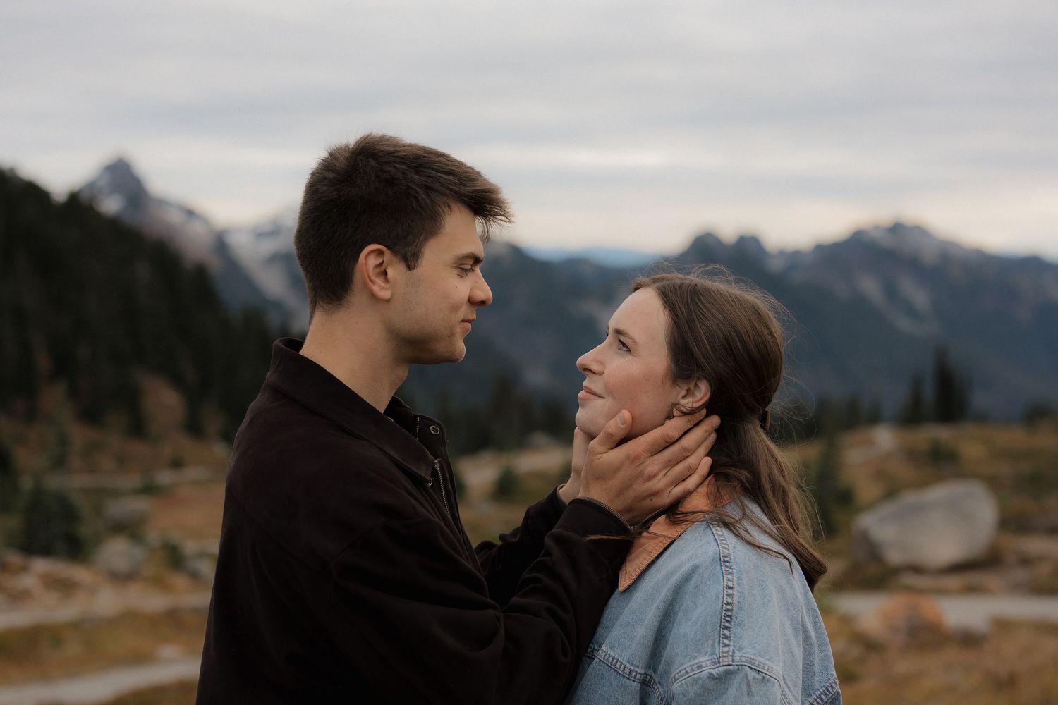 Couple sharing a tender moment with mountain landscape backdrop, man gently holding woman's face.
