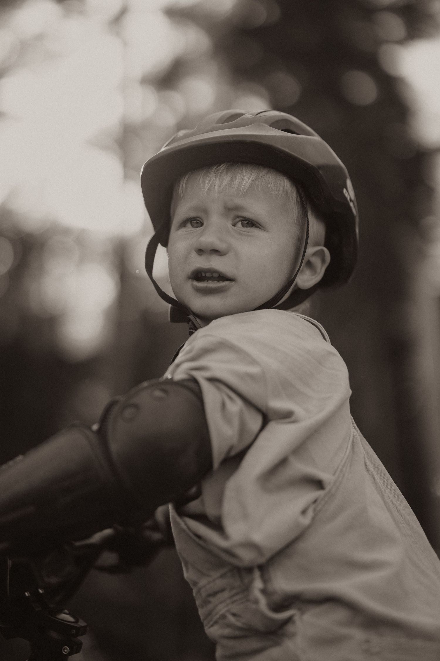 Young boy wearing a bicycle helmet rides a bike outdoors in a sepia-toned vintage-style portrait photo.