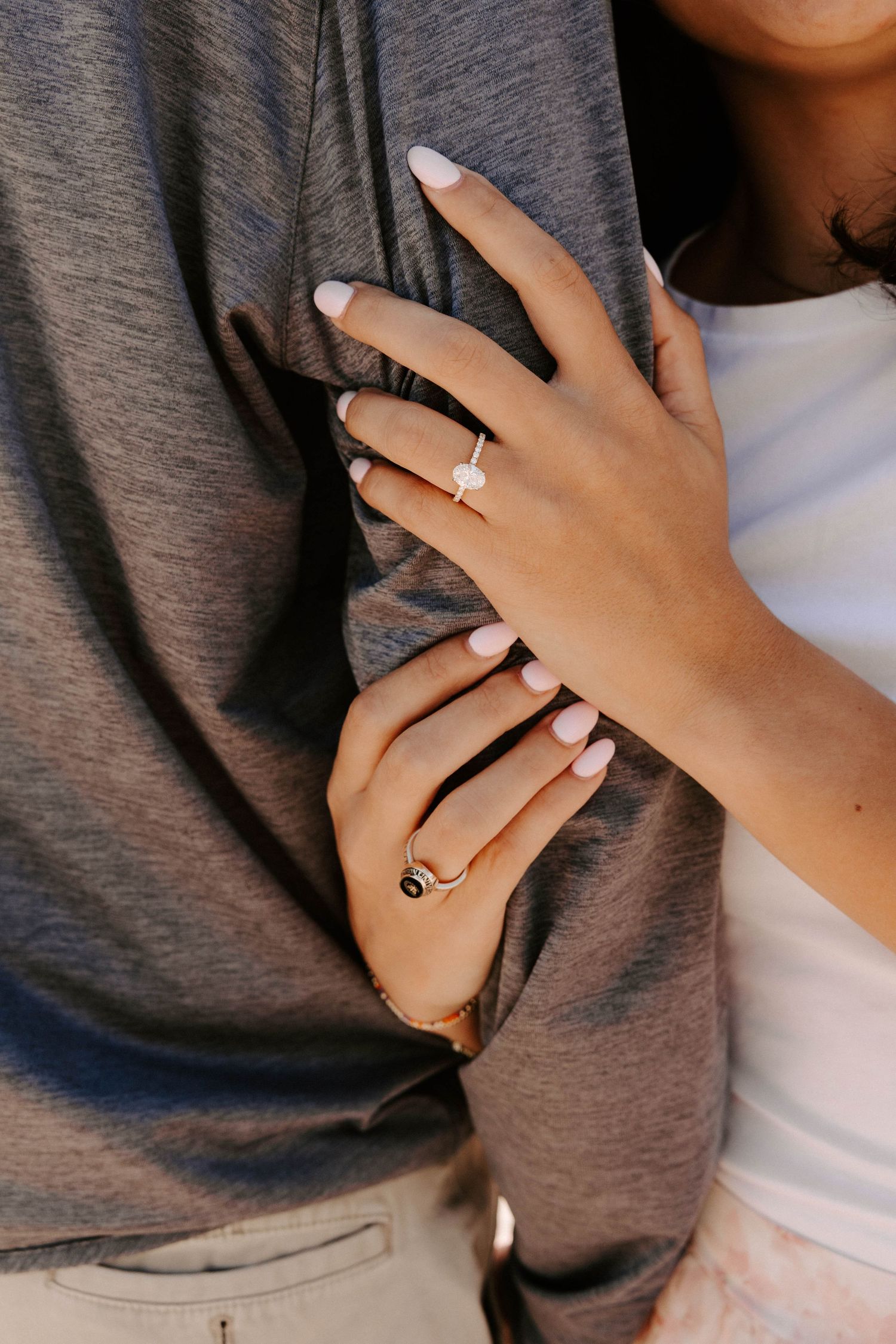 Close-up of a woman's hands showing a diamond engagement ring while embracing a man in a gray shirt.