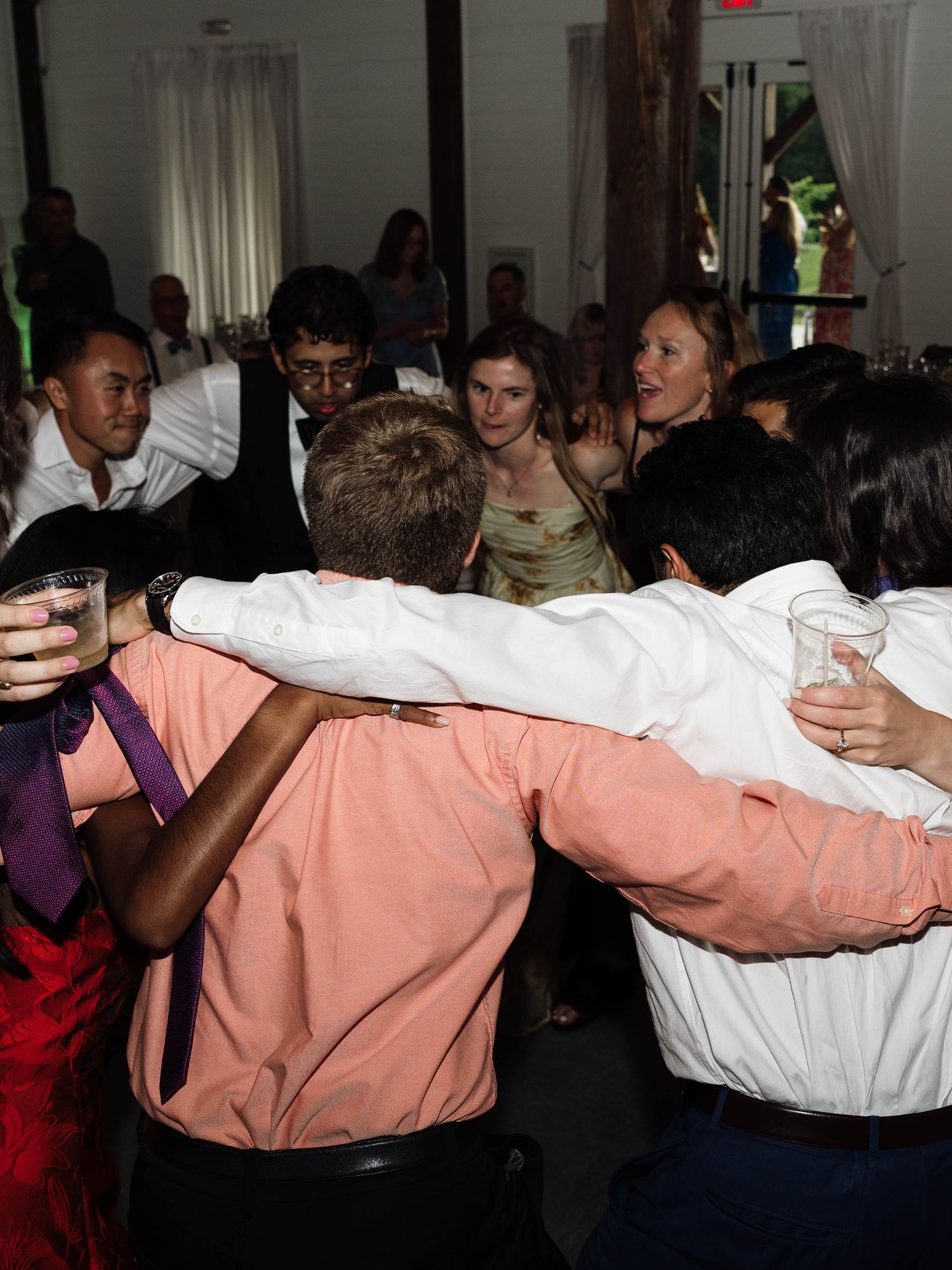Young wedding guests dancing together in a circle at a lively indoor wedding reception celebration.