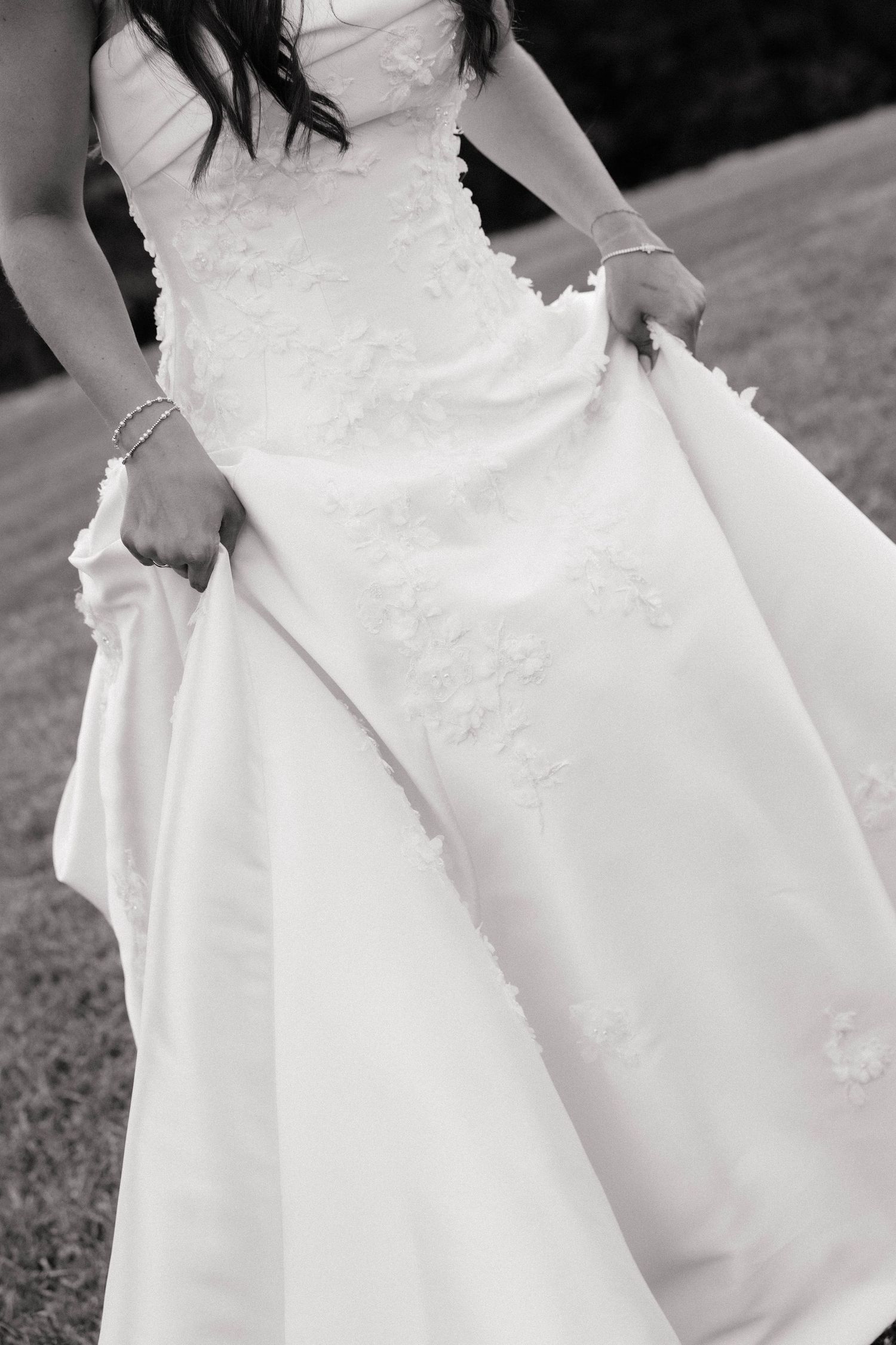 Black and white close-up of a bride in a floral applique strapless wedding gown holding her skirt.