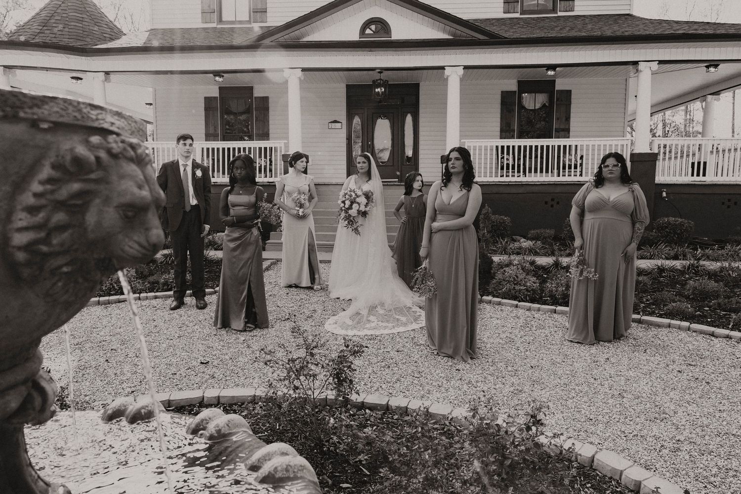 Wedding party poses in front of elegant white manor house in black and white photo.