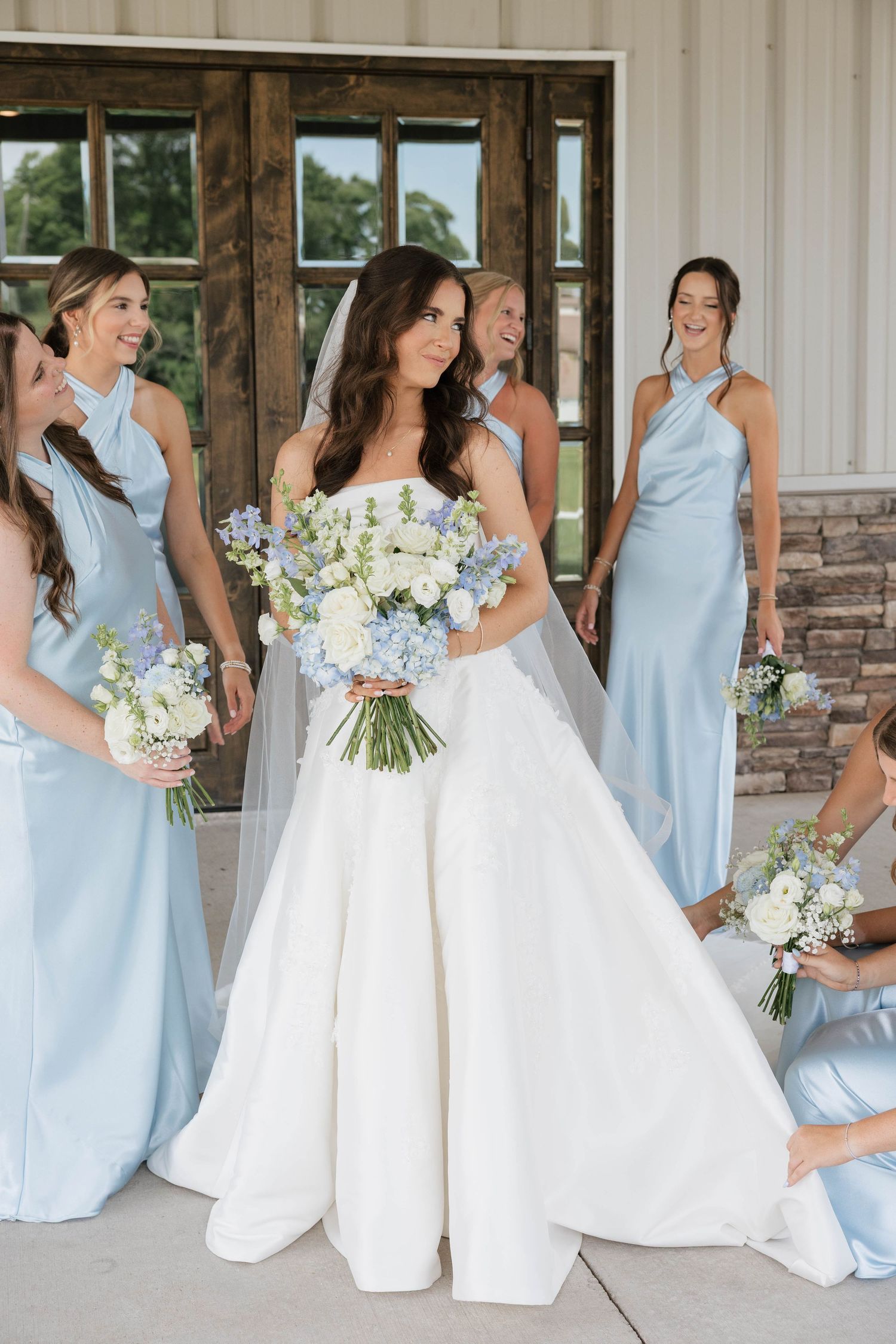 A radiant bride in a white ball gown holds a blue and white bouquet surrounded by light blue bridesmaids.