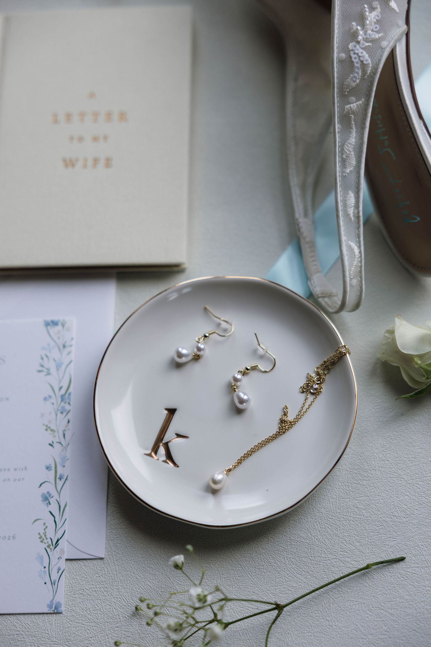 Elegant bridal jewelry flat lay with pearl earrings, gold necklace on monogram dish with wedding stationery.