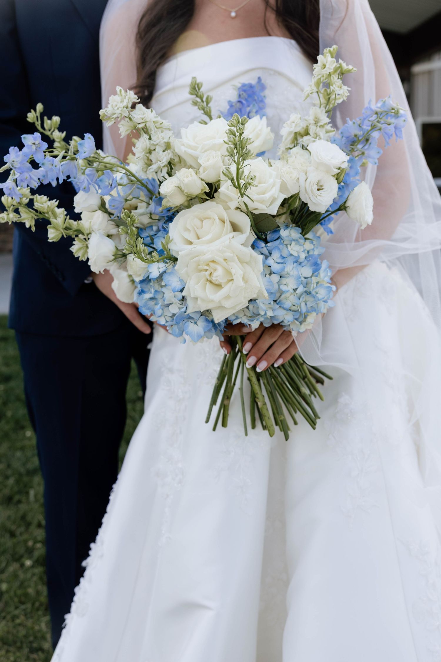 Bride holding a stunning blue and white wedding bouquet featuring hydrangeas and roses in a white gown.