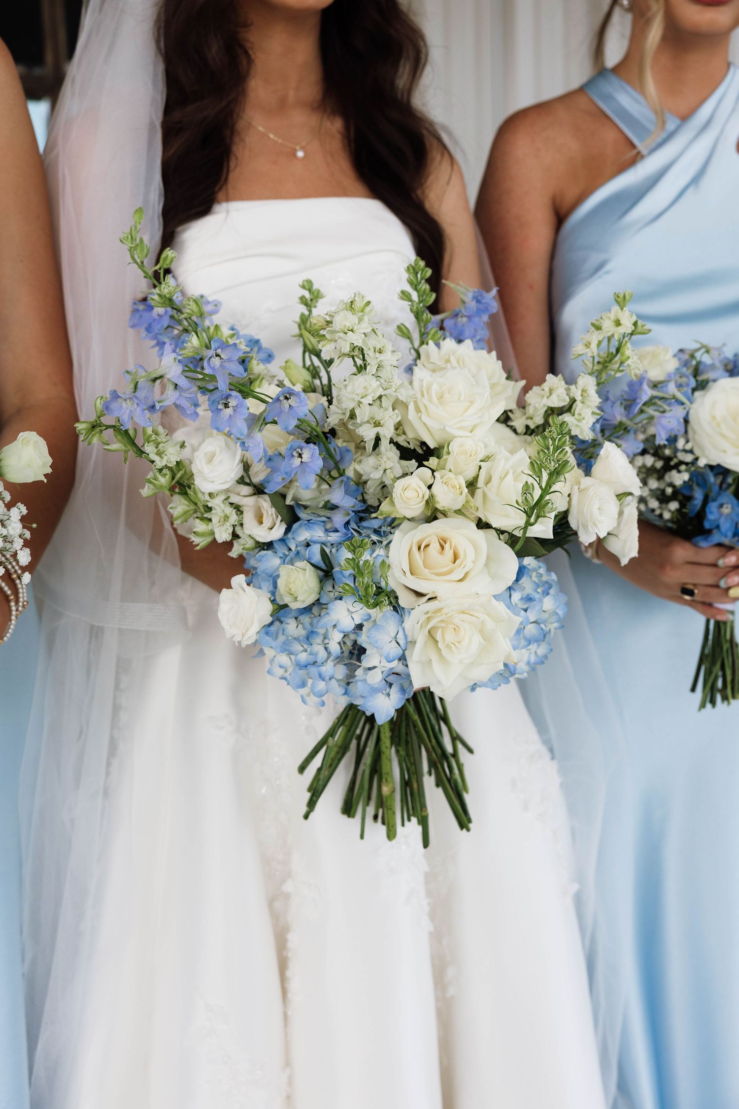 A bride in a strapless white gown holds a stunning blue hydrangea and white rose wedding bouquet.