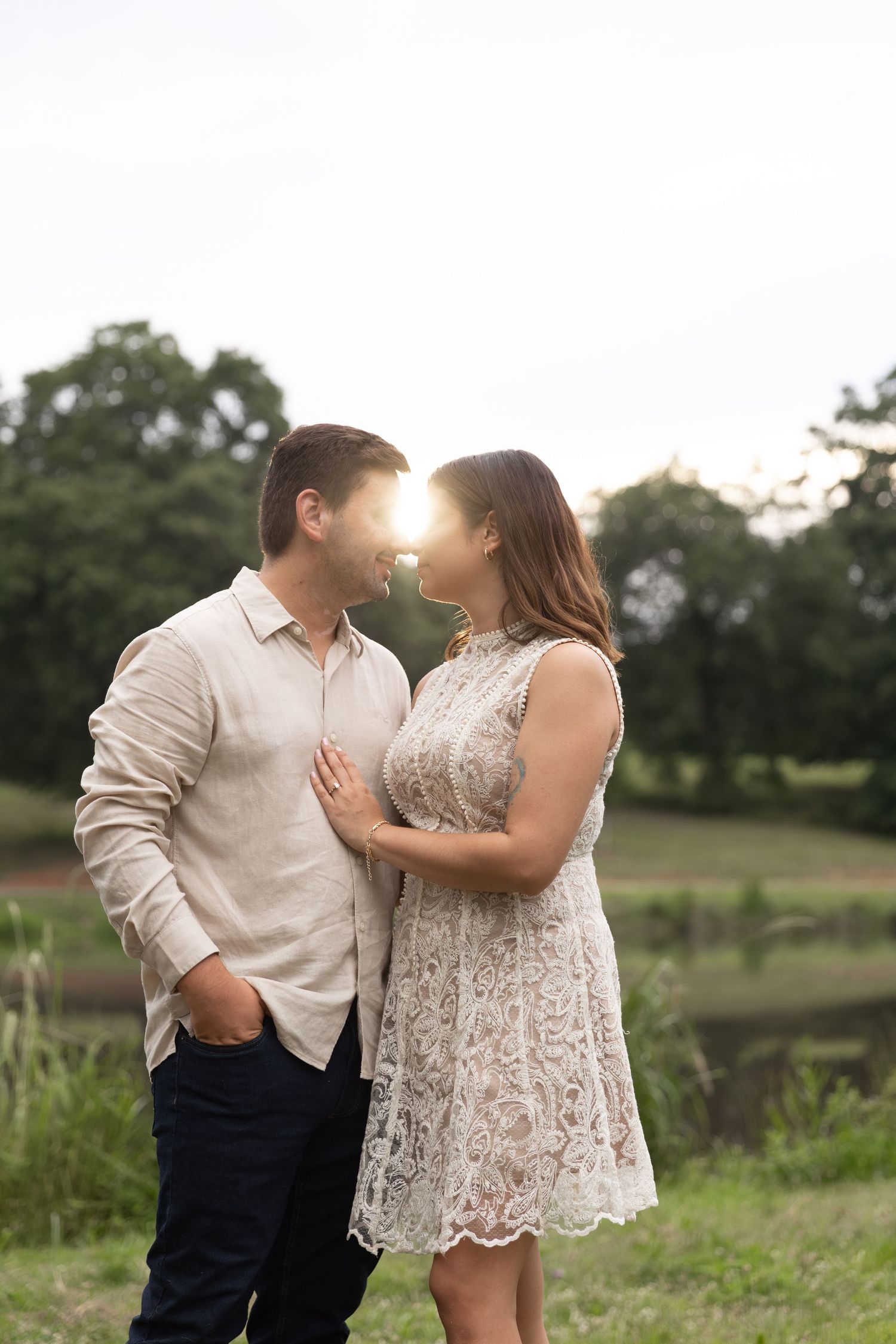 Couple sharing a romantic moment outdoors at sunset, woman in lace dress and man in linen shirt, surrounded by lush greenery.
