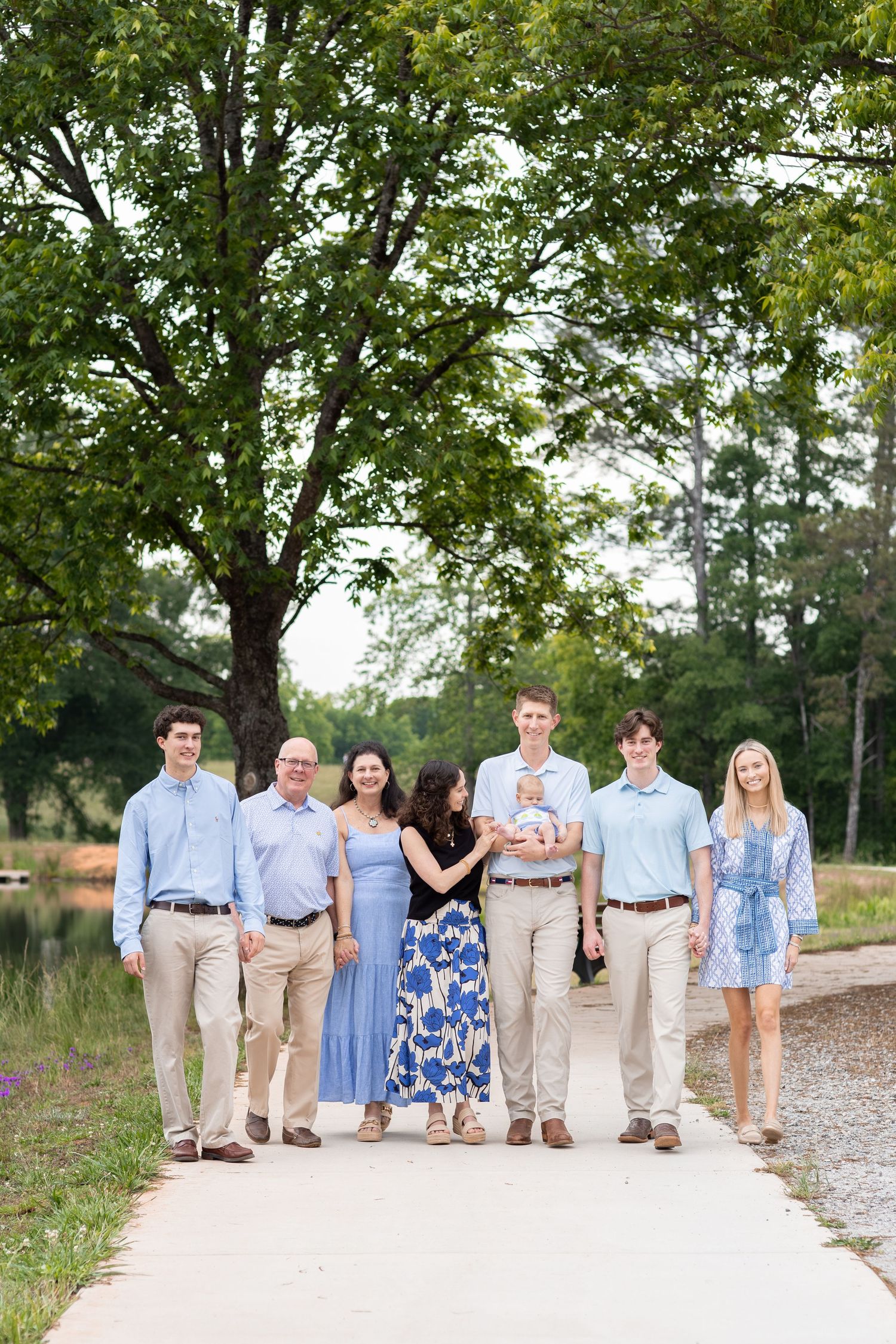 Family of seven poses on a pathway surrounded by trees during an outdoor photo session.