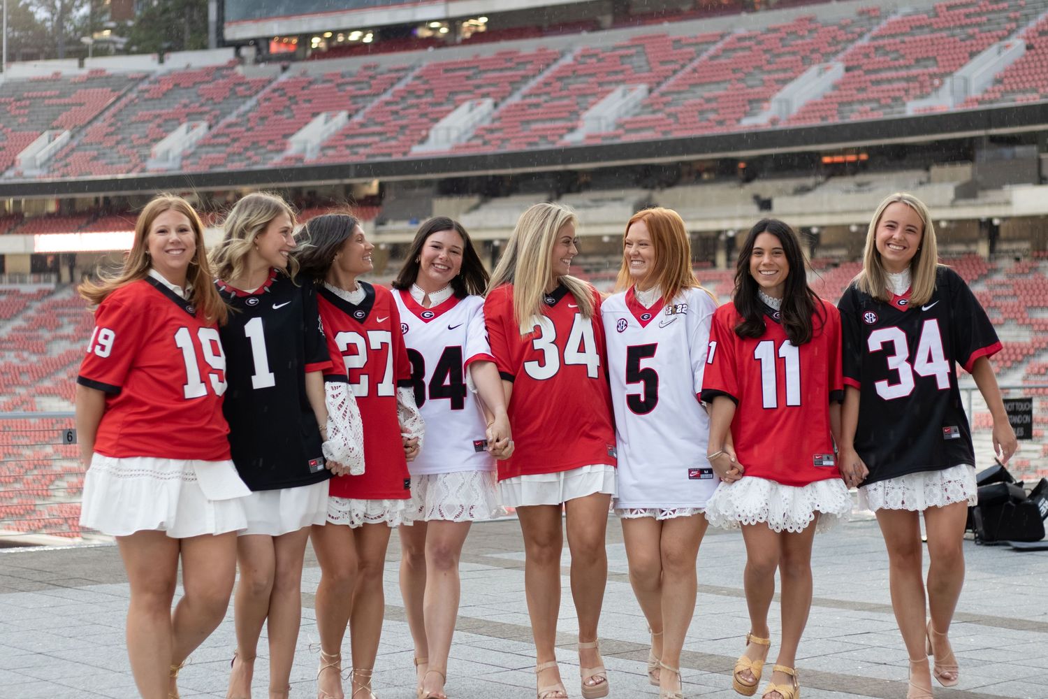 Group of women wearing football jerseys posing together on a stadium field, smiling for a photo.