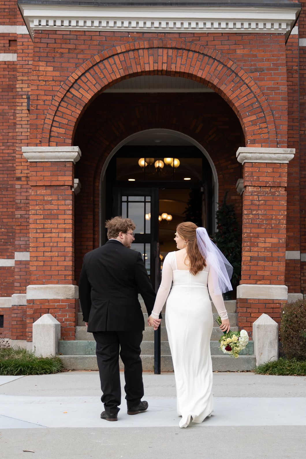 Bride and groom holding hands walking toward a red brick church entrance on their wedding day.