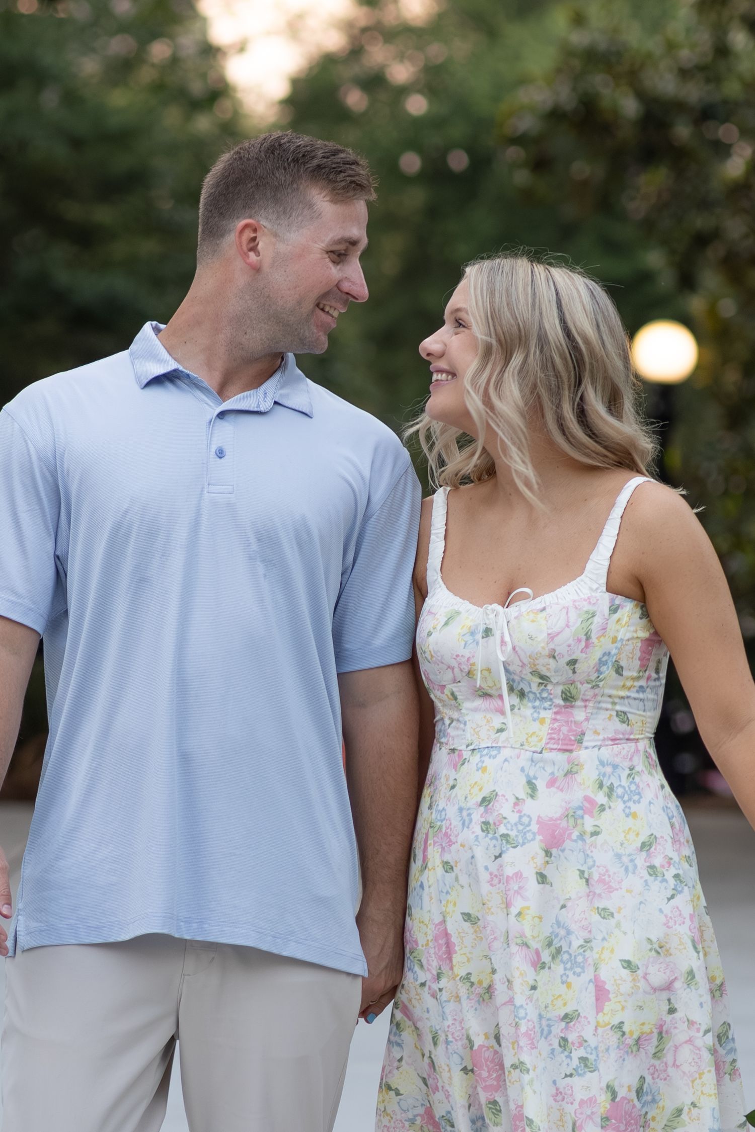 Smiling couple holds hands and gazes at each other during outdoor pregnancy announcement shoot.