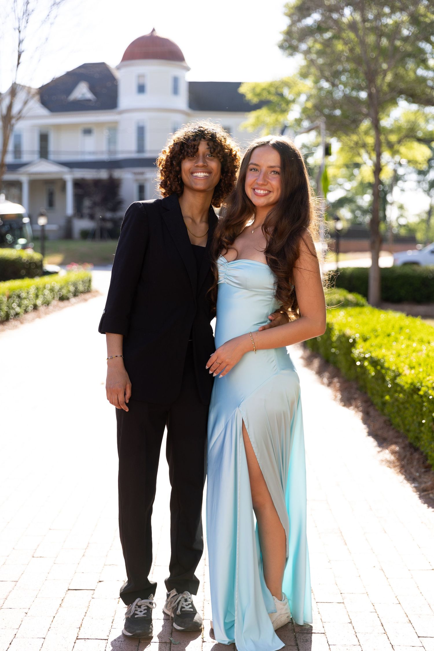 Young couple in formal prom attire posing outdoors, woman in light blue gown and man in black suit.