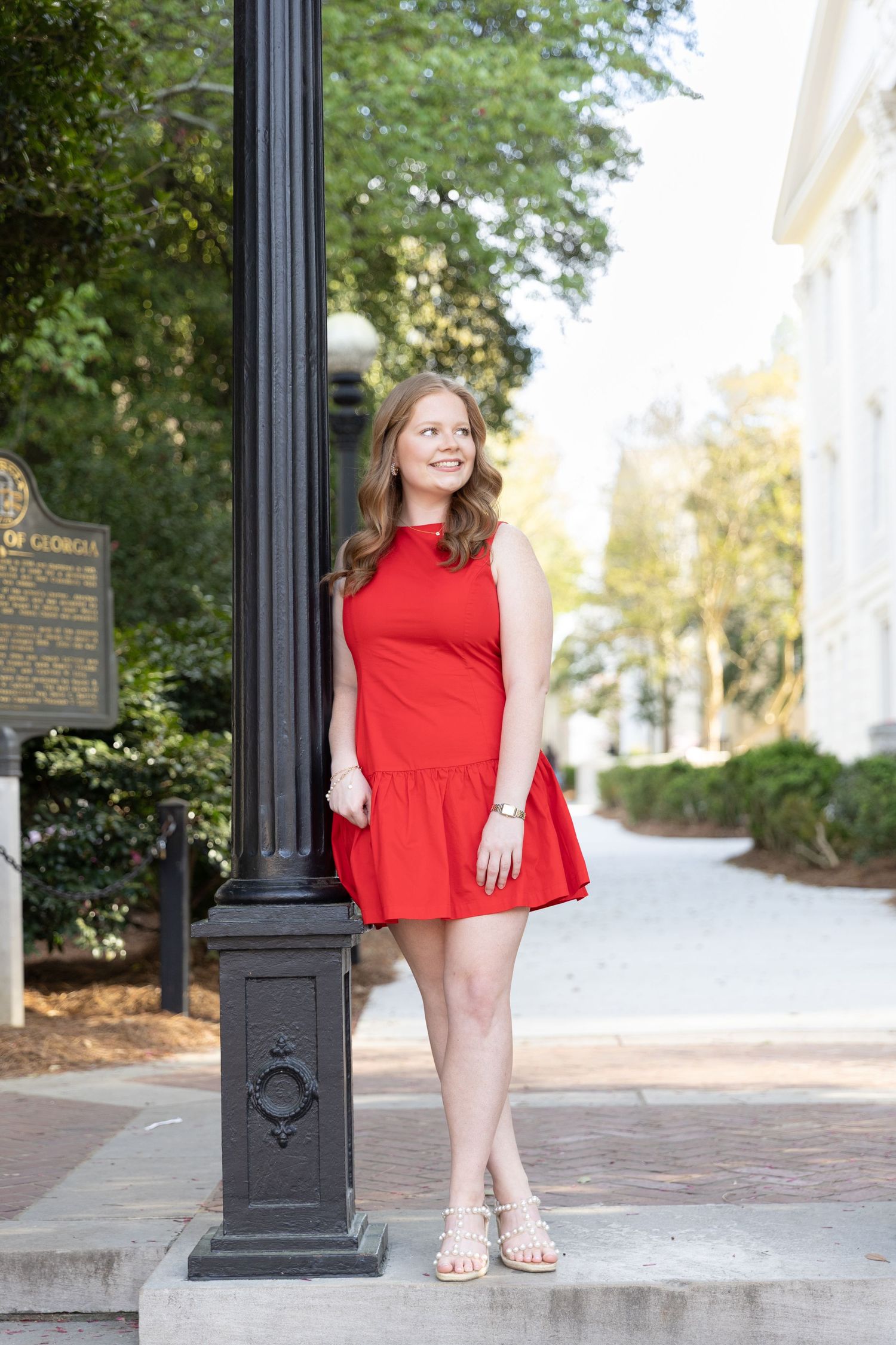 Young woman in red dress posing by black lamp post on brick sidewalk near historic building.