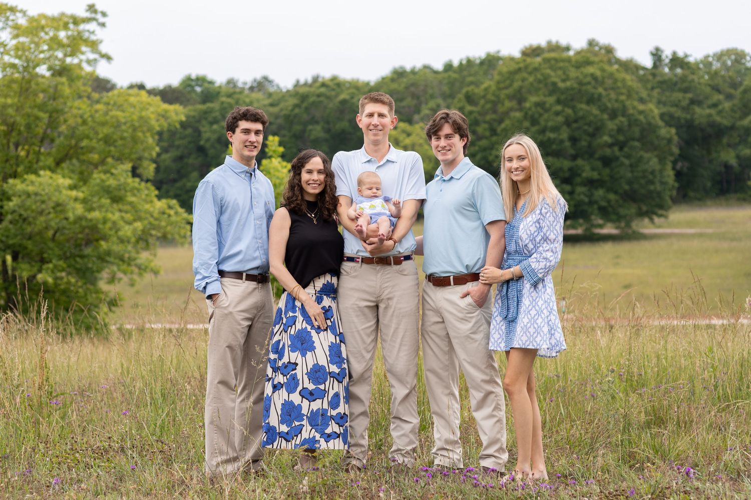 Family of six posing outdoors in a green meadow, dressed in casual summer attire for a professional portrait.