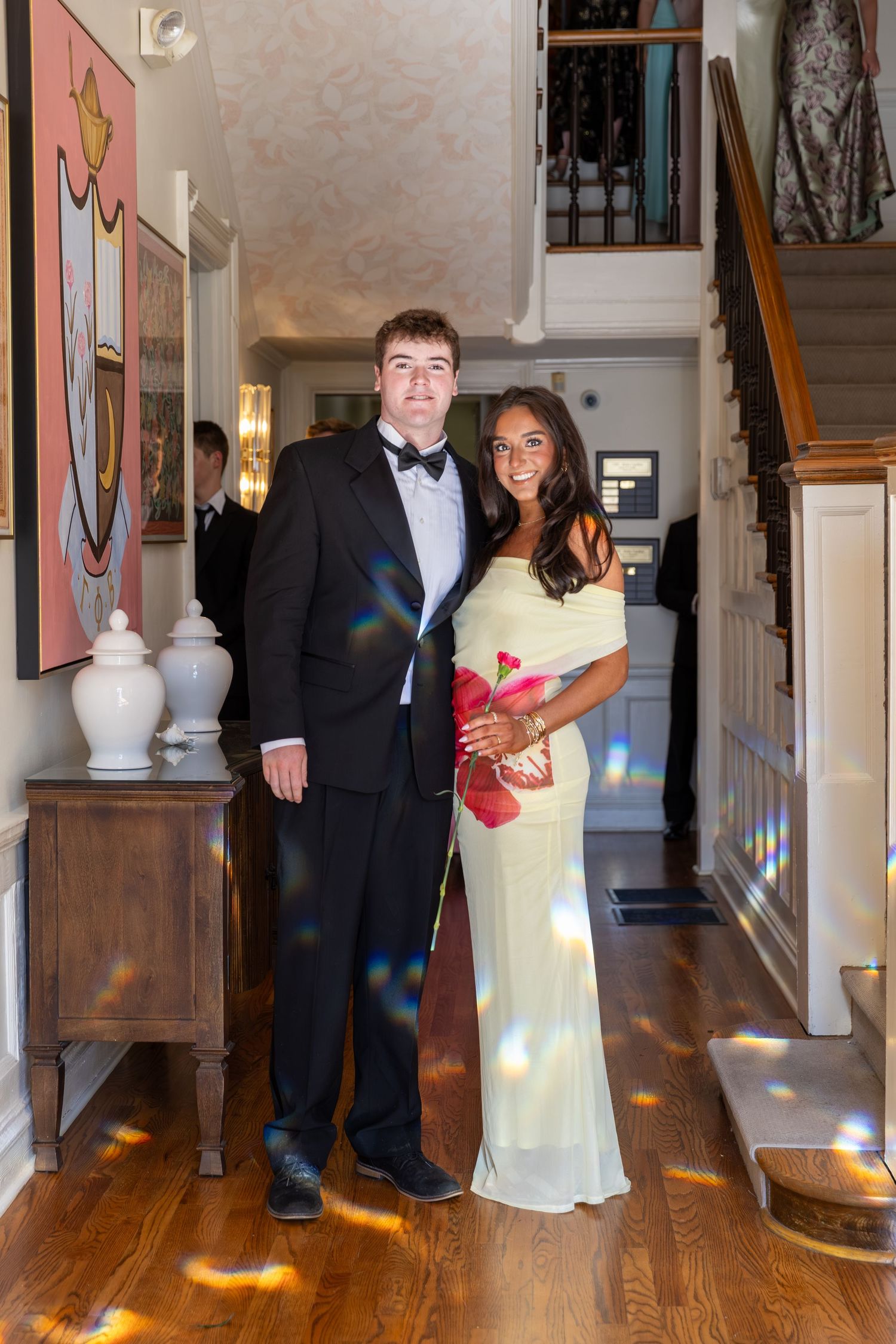 A young couple dressed in formal attire poses in an elegant home hallway for prom.