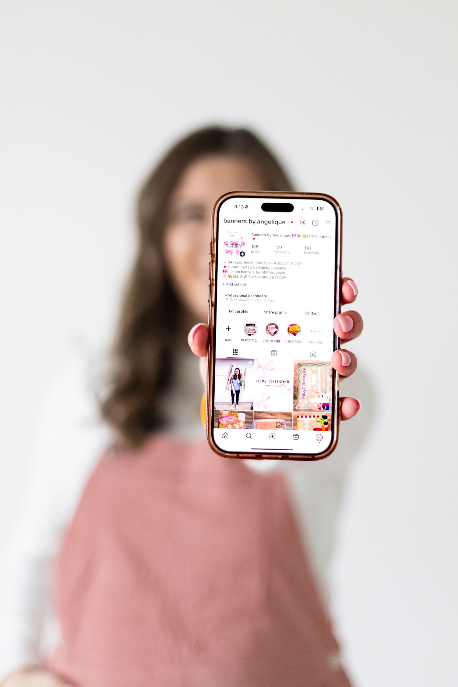 Woman holding iPhone displaying a pink Instagram profile page with posts and highlights visible on screen.