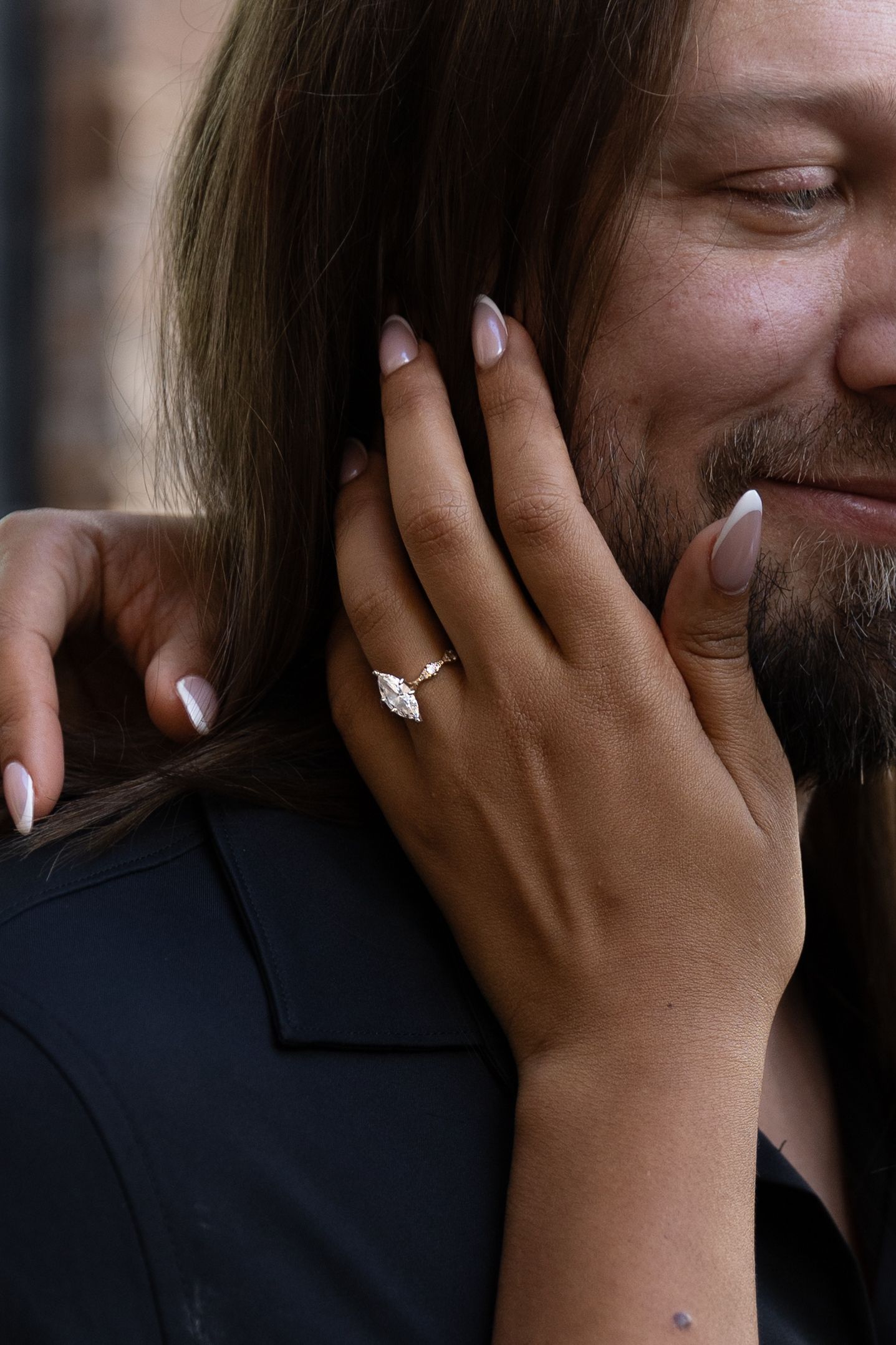 Close-up of a woman's hand with nude nails wearing a marquise diamond engagement ring on a gold band.