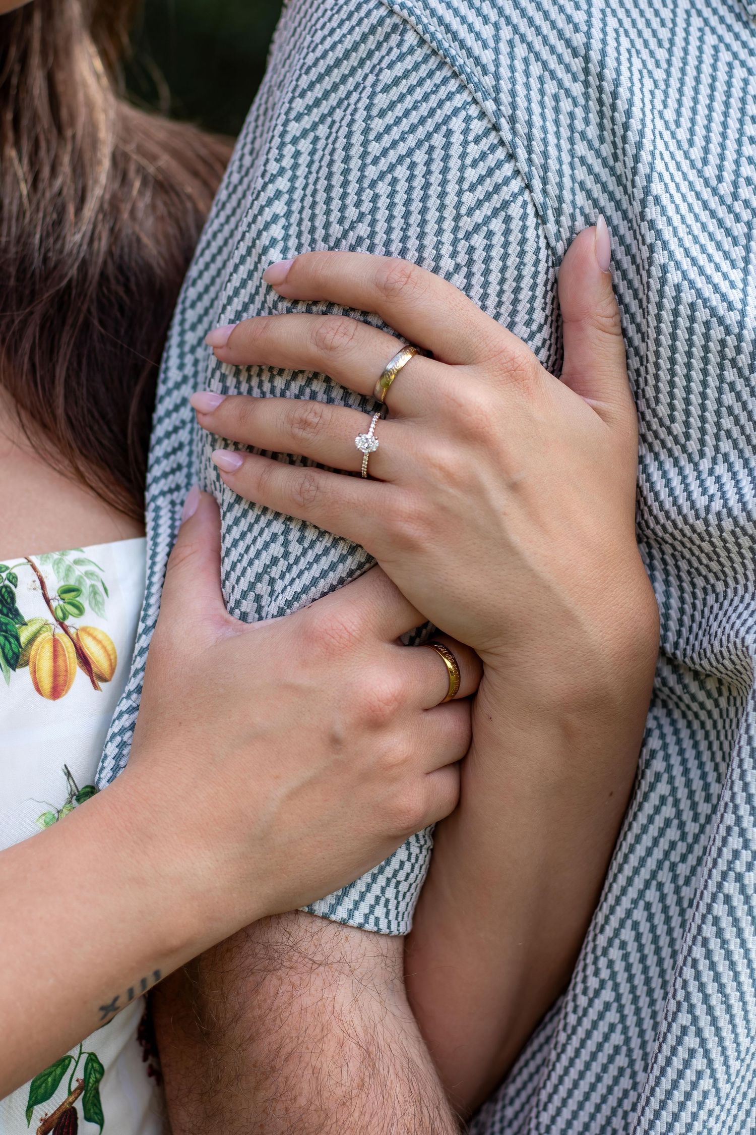Couple embracing, woman wearing a diamond engagement ring and gold band on her finger, man wearing a gold wedding band.