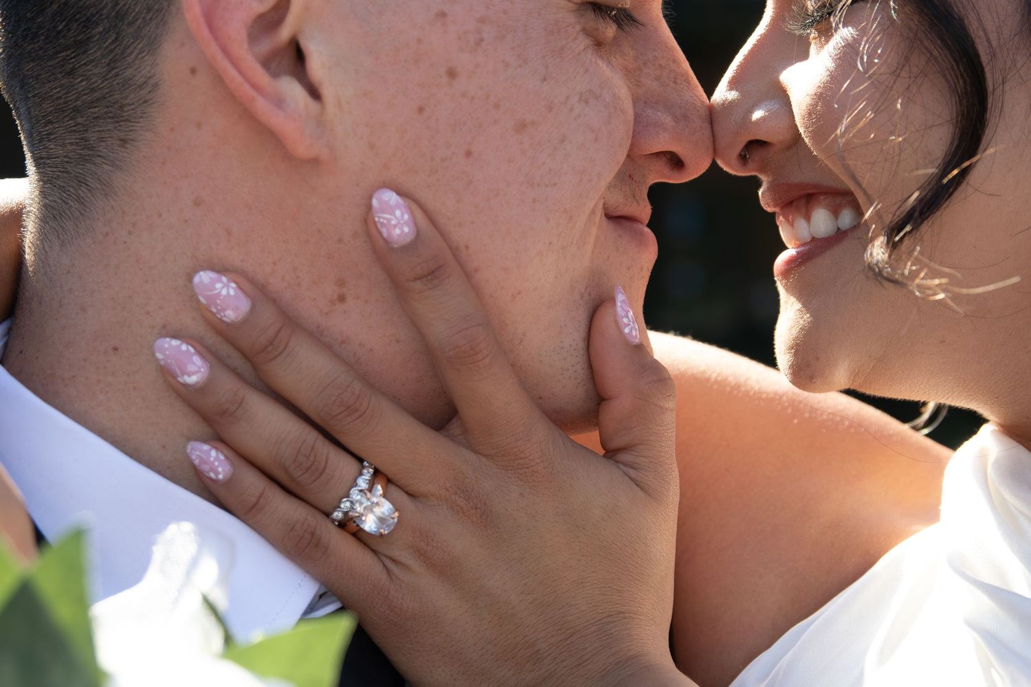 Close-up of a bride and groom almost kissing, showcasing a diamond engagement ring on the bride's hand.