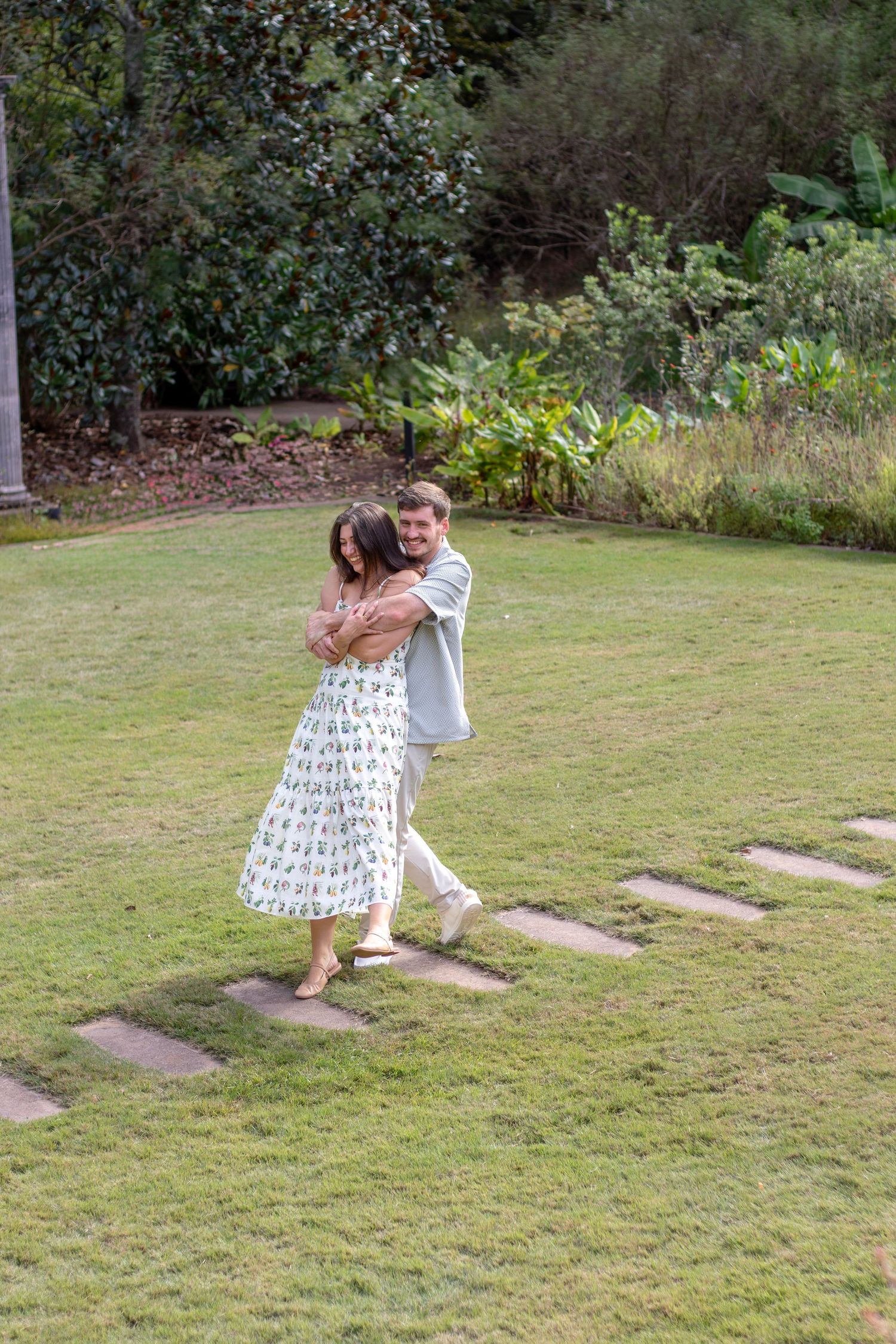 Couple embracing and dancing together on a lush green lawn surrounded by tropical garden greenery.