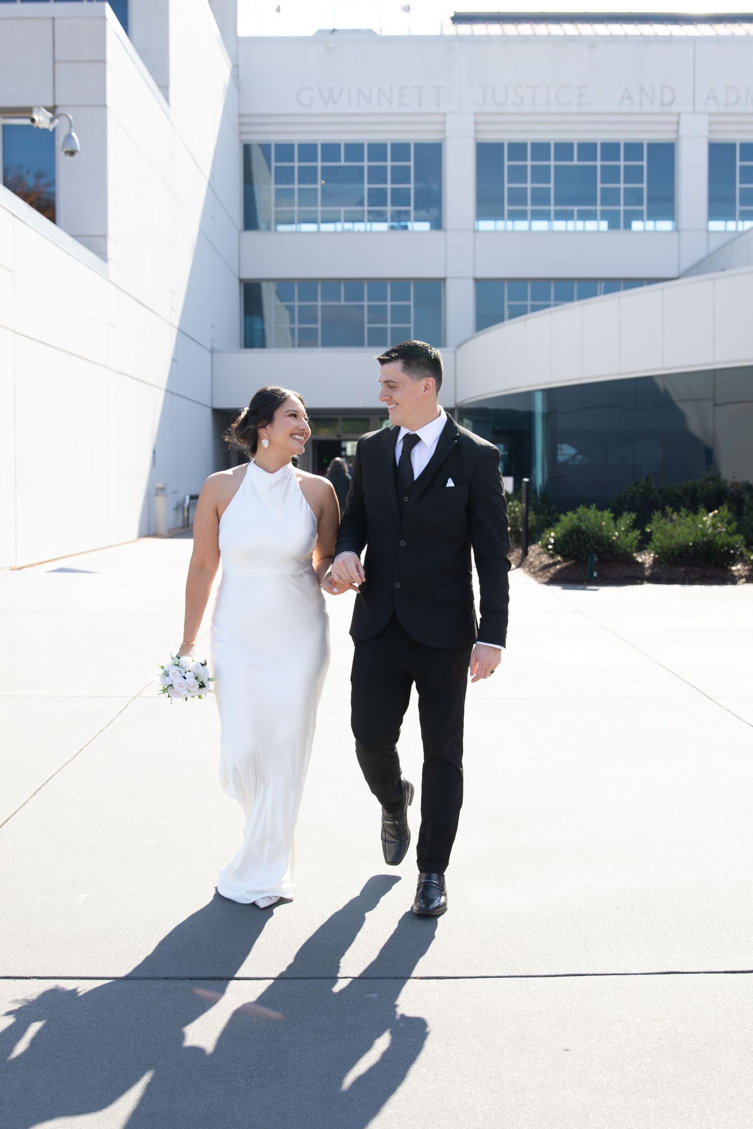 Bride and groom walk hand-in-hand outside Gwinnett Justice Center on their wedding day.