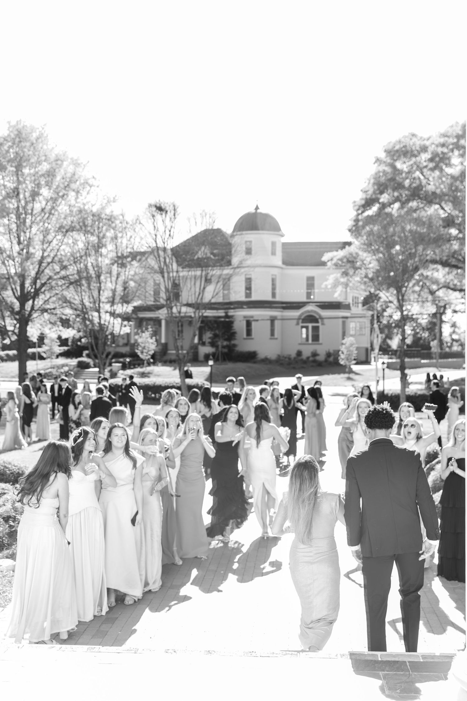 Black and white photo of a large group of prom attendees gathered outside a historic building.