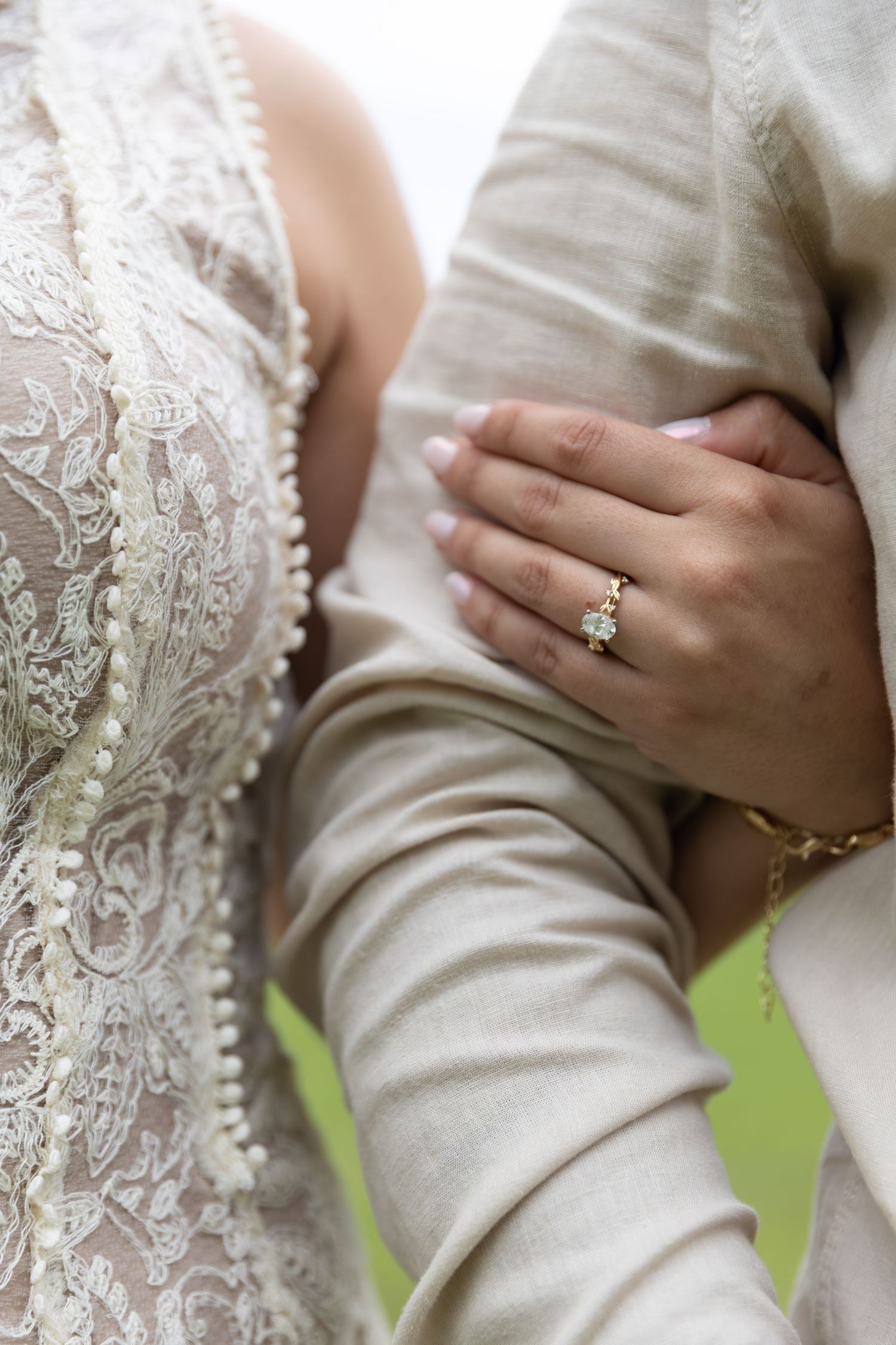 Close-up of bride in lace wedding dress holding groom's arm, showcasing elegant diamond engagement ring.