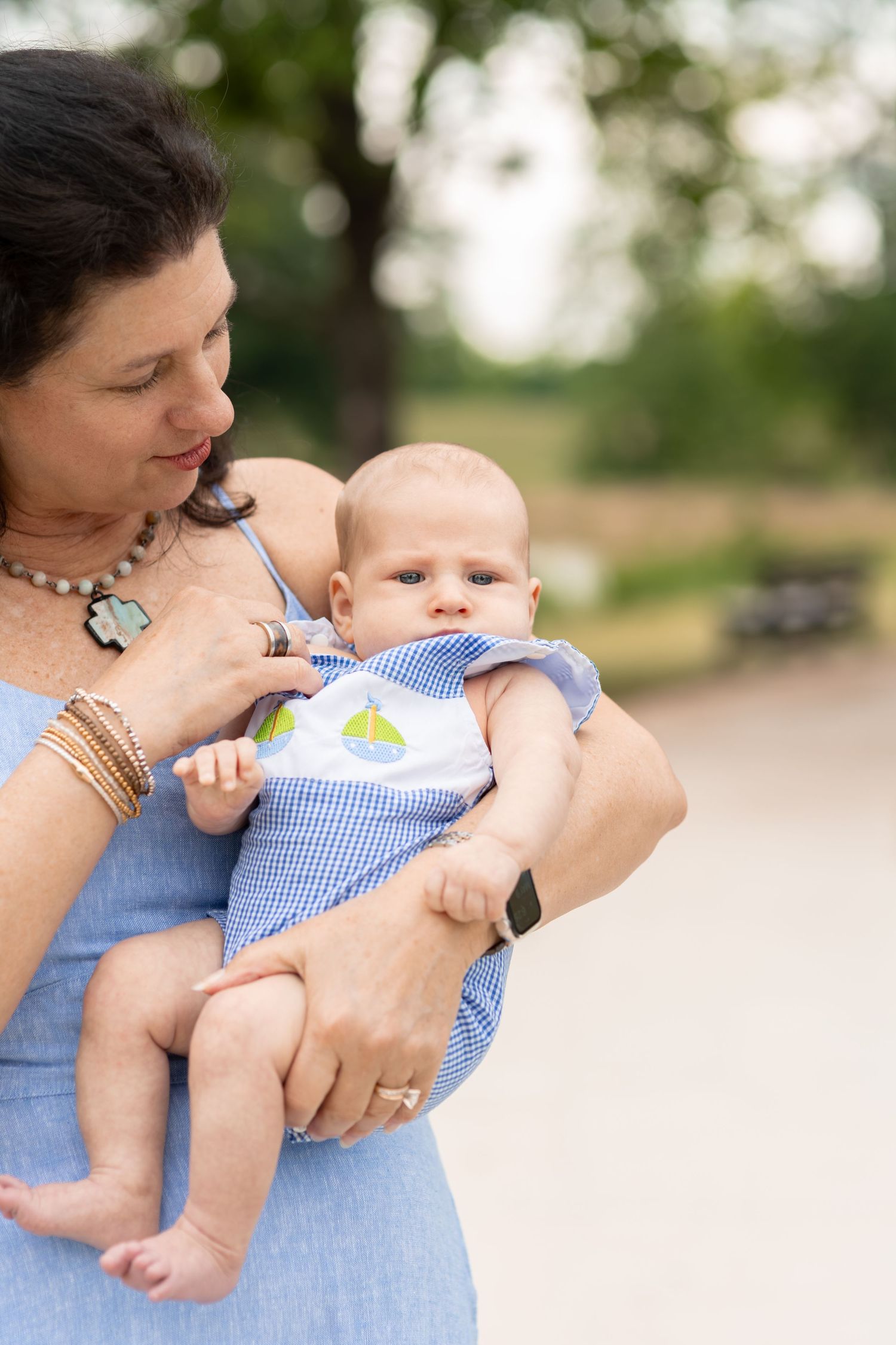 Grandmother in blue dress lovingly holds her baby grandchild outdoors in a park.