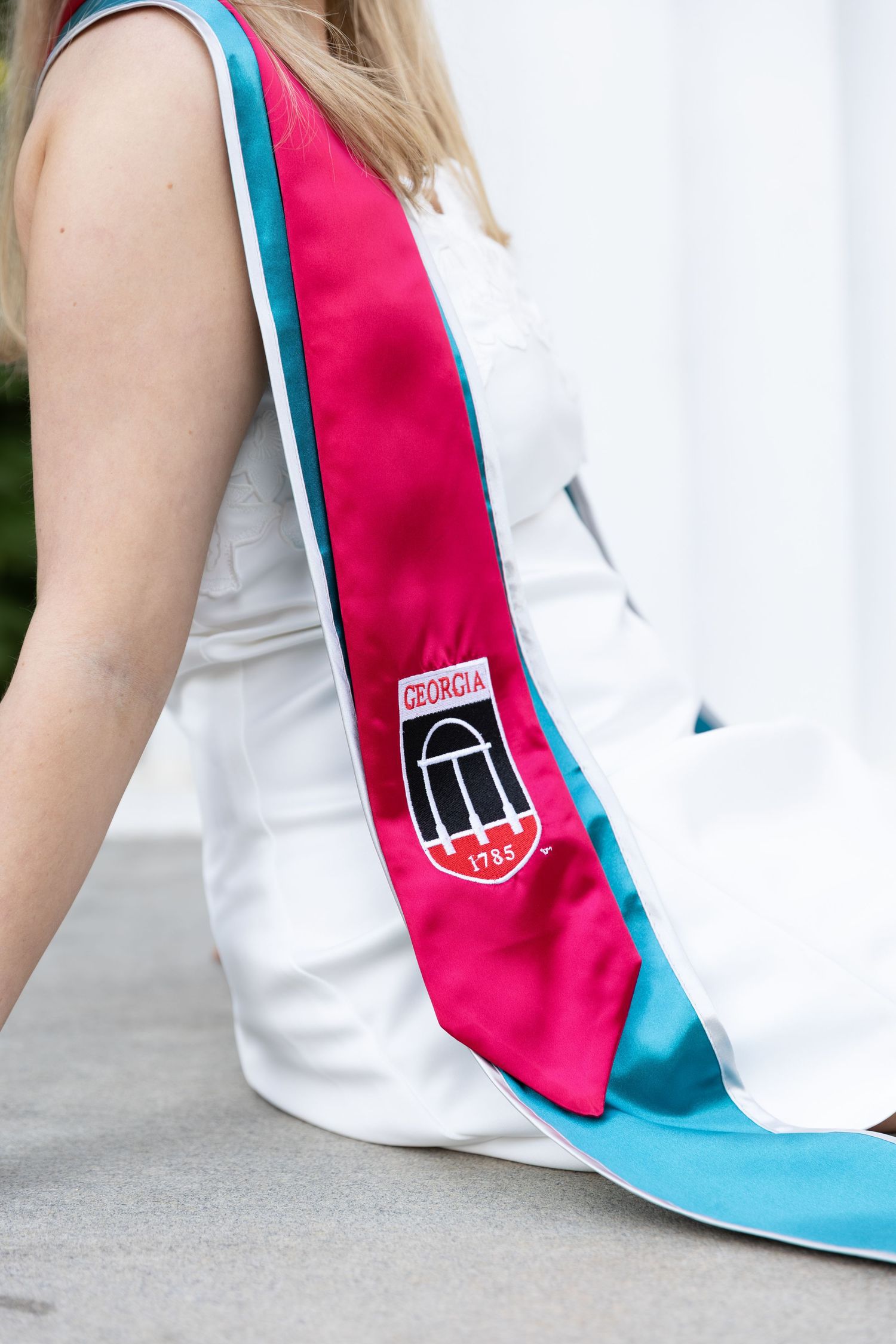 University of Georgia graduation stole in red and teal with UGA arch logo, worn over white dress.