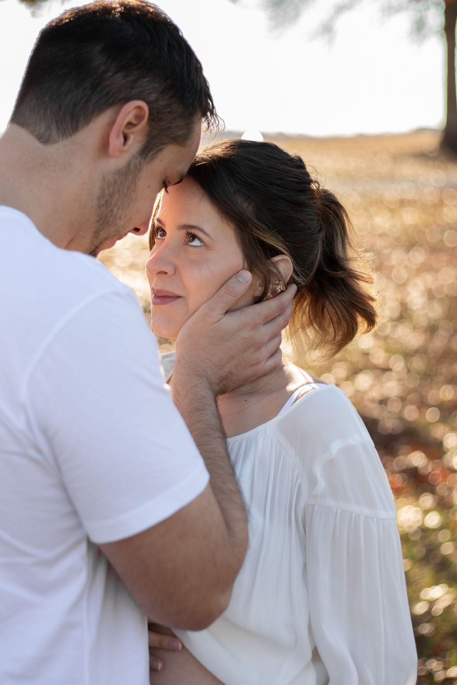A man tenderly holds a woman's face as she gazes up at him outdoors in warm golden light.