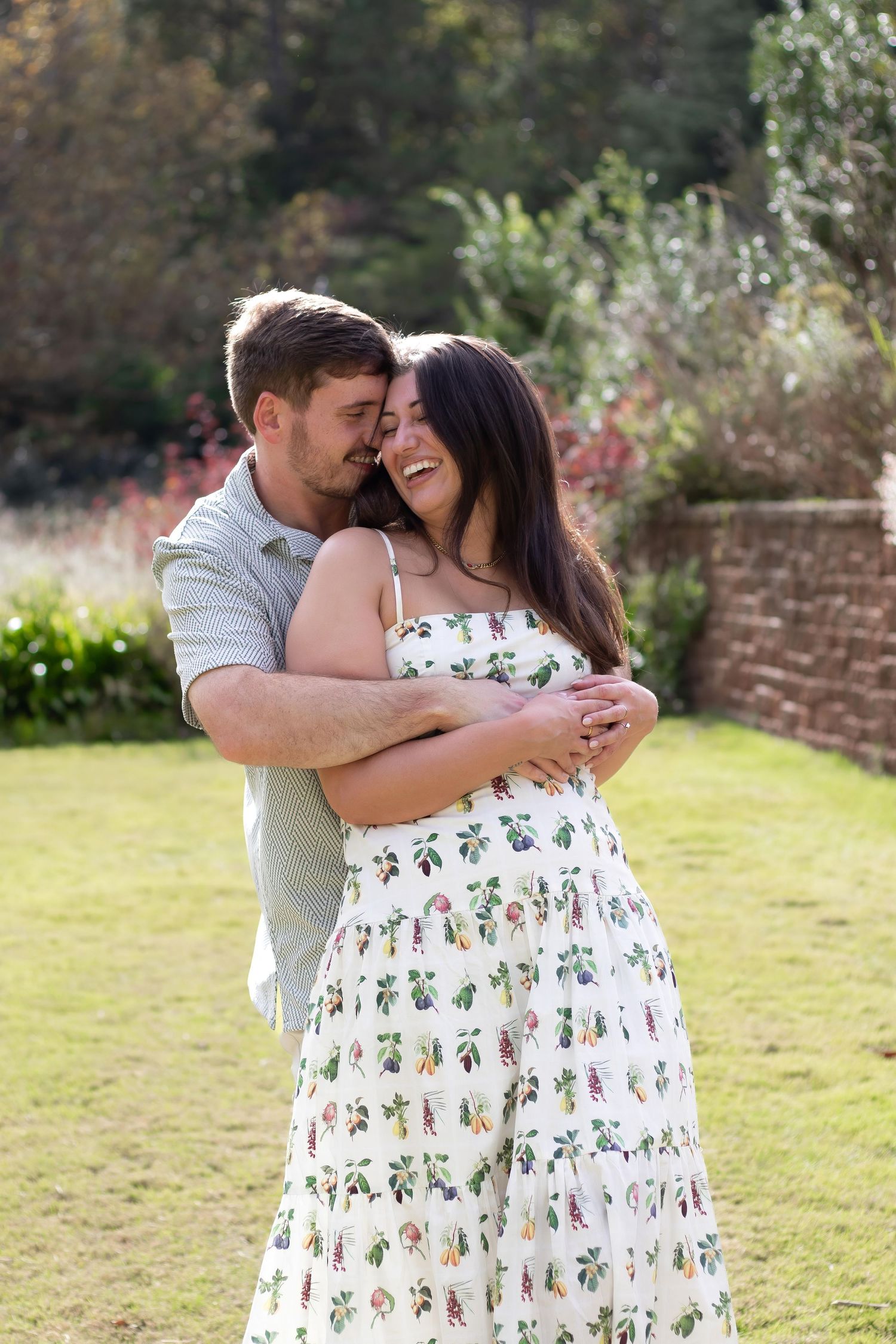 Happy couple hugging and laughing together on a sunny green lawn with garden backdrop.