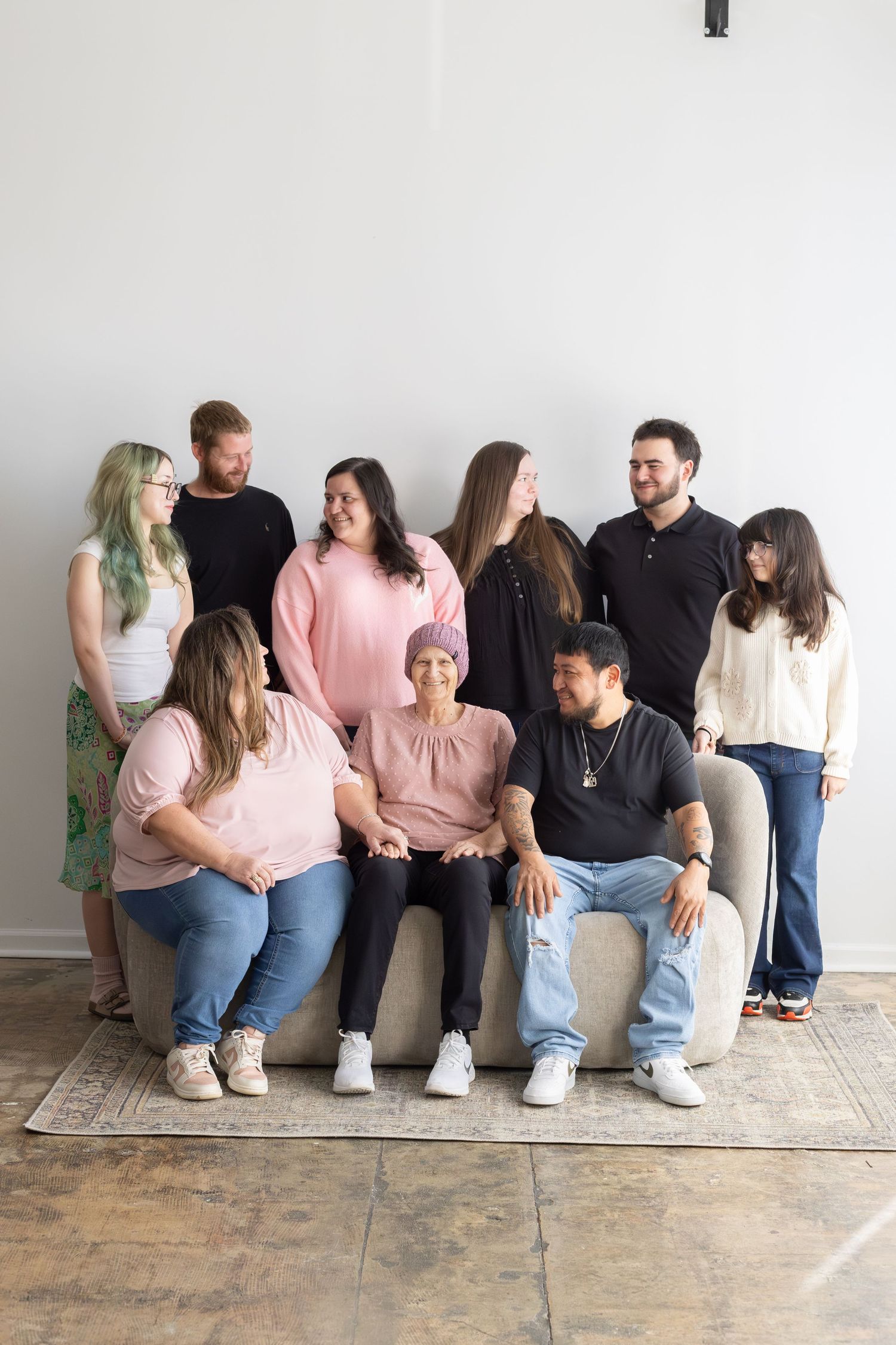A family of nine poses together on a couch, smiling warmly, with one woman wearing a teal headscarf in the center.