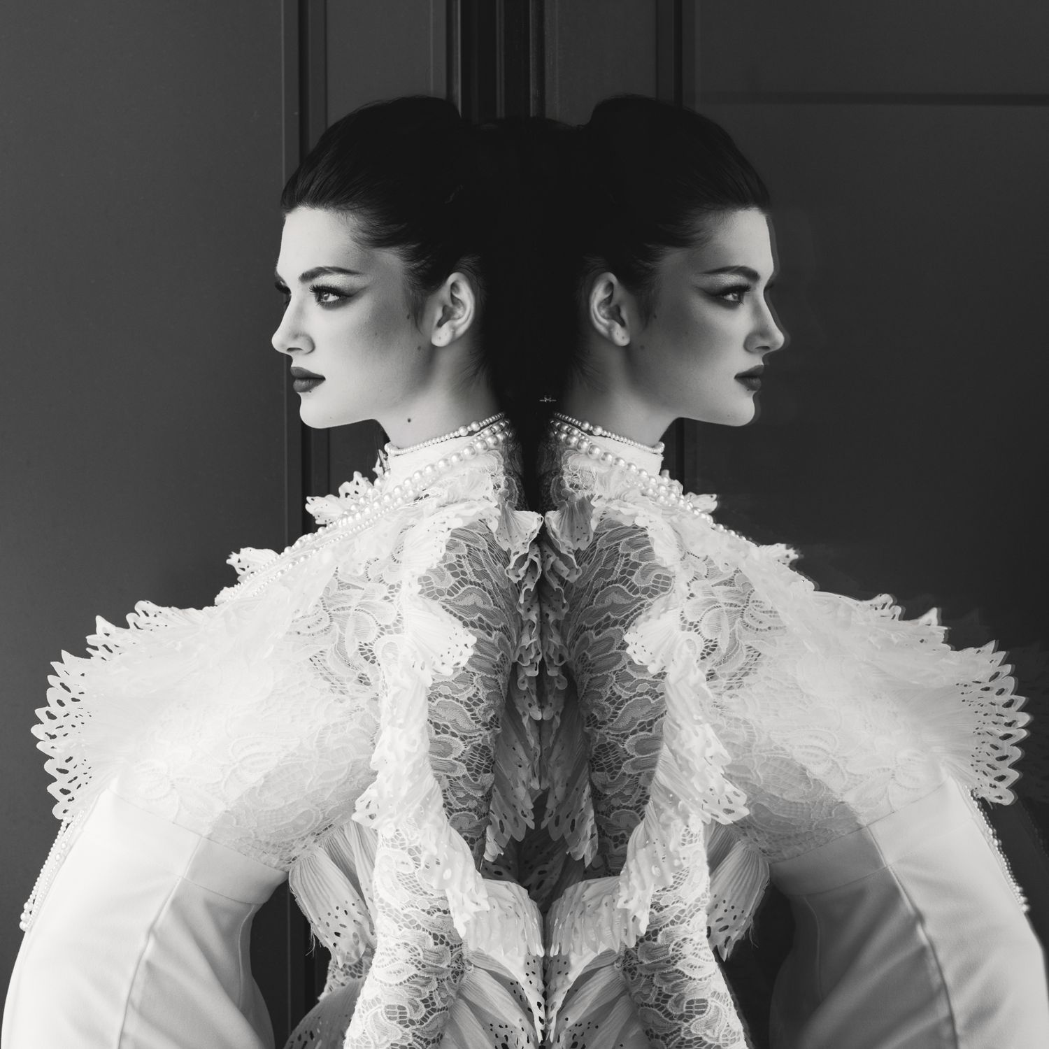 Black and white mirror reflection of woman in ornate white lace Victorian-style gown.