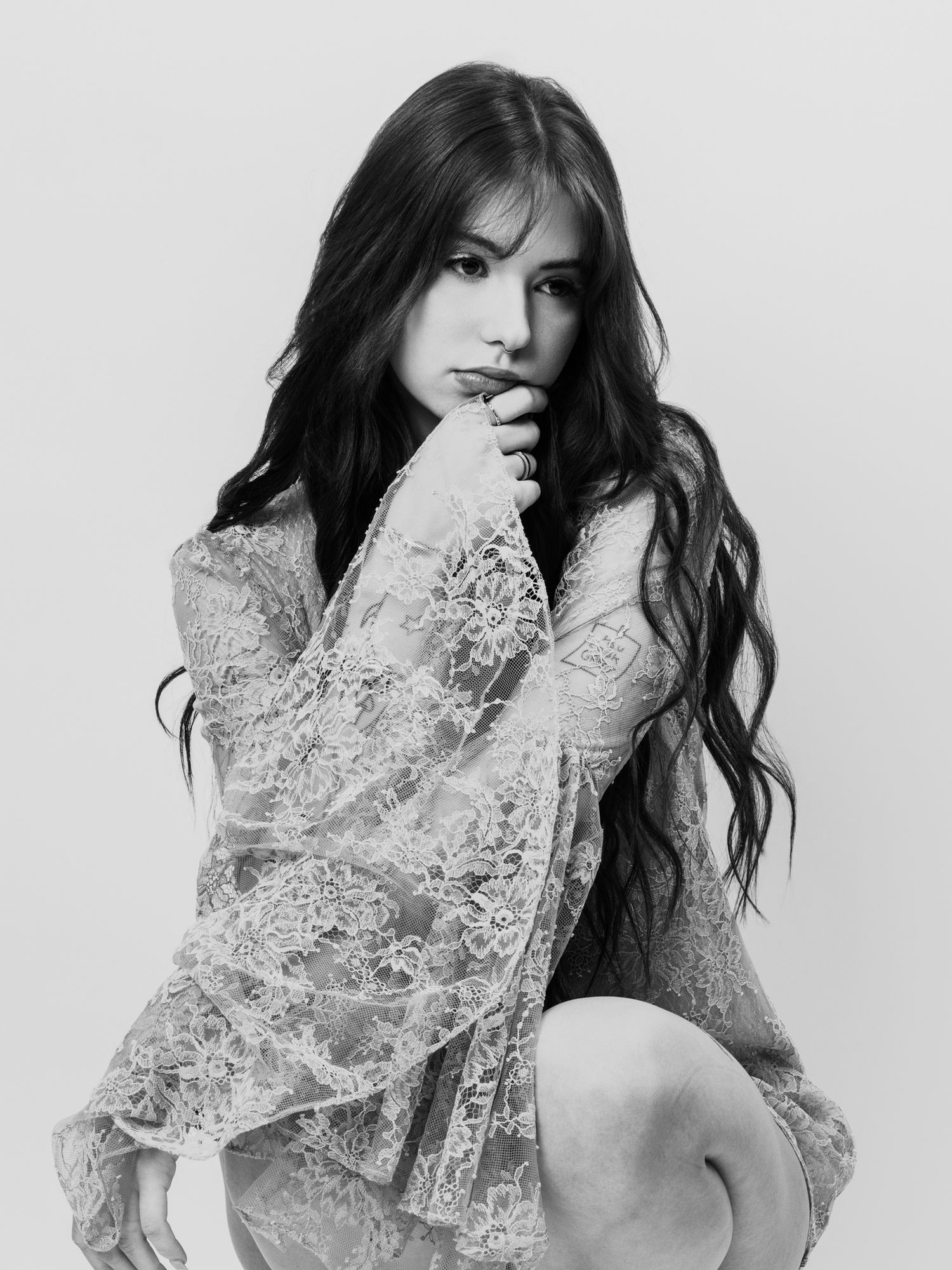 Black and white portrait of a young woman with long dark hair wearing a lace dress, posing elegantly.